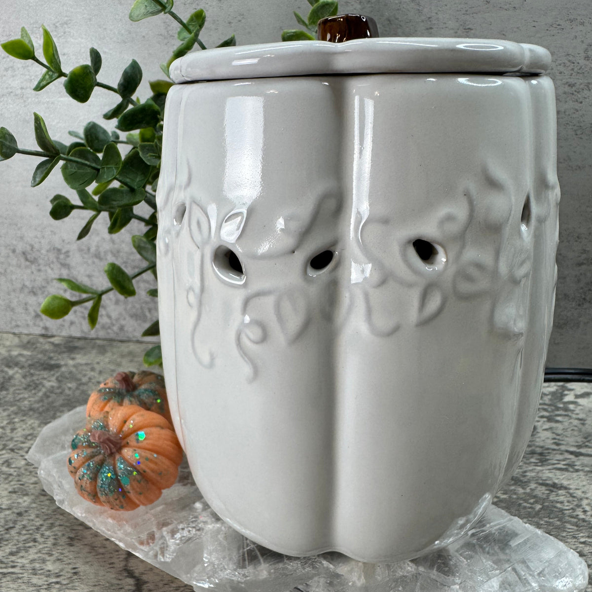 Decorative white ceramic planter with tree design on a gray surface with greenery and a small pumpkin.
