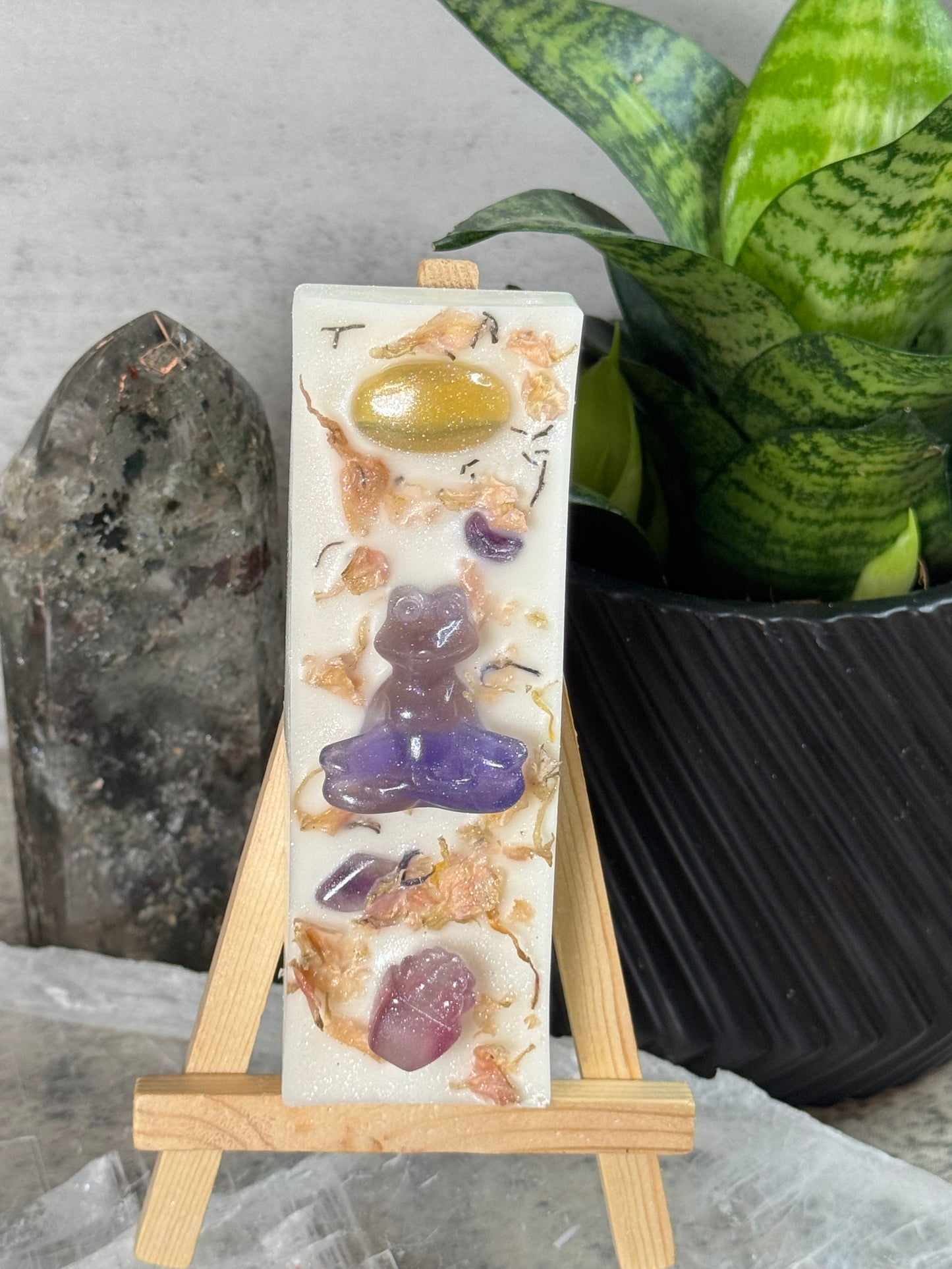 Decorative soap bar with embedded stones on a stand, surrounded by plants and rocks.