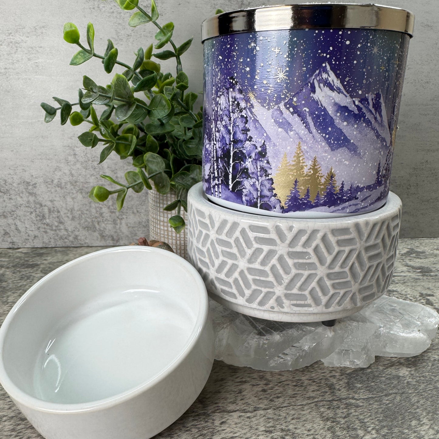 Decorative candle with geometric design and plant on a textured surface