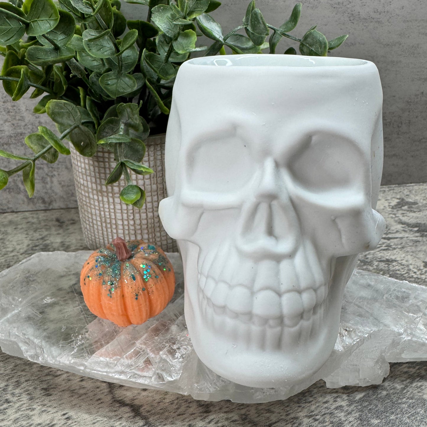 White ceramic skull with a small pumpkin and greenery on a stone surface