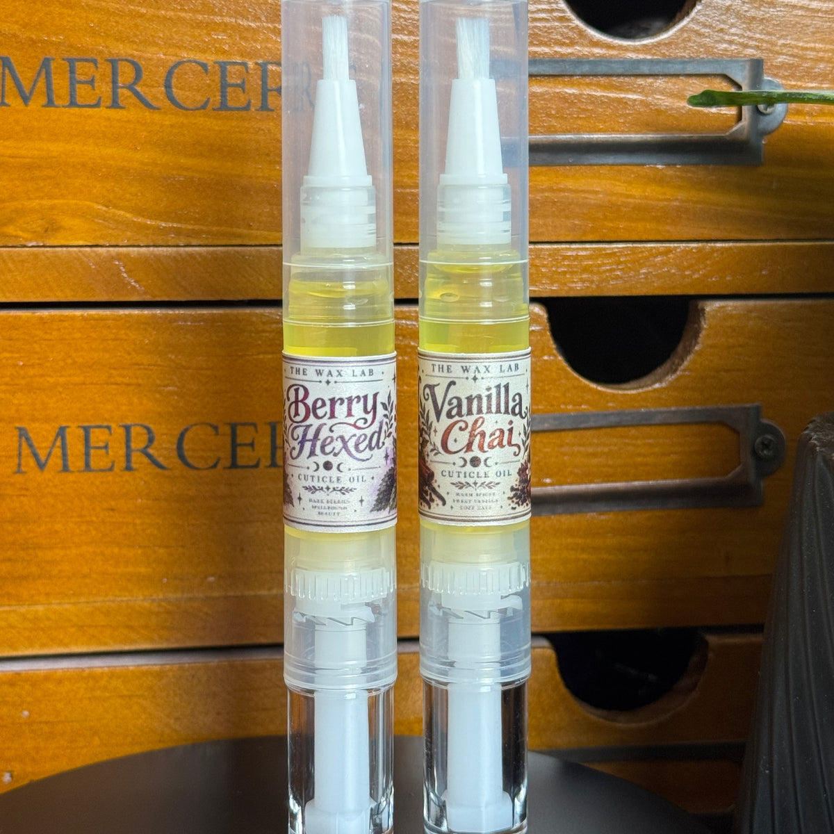 Two clear plastic spray bottles of Vanilla Chai and Berry's Haze essential oils resting on a wooden slatted surface.