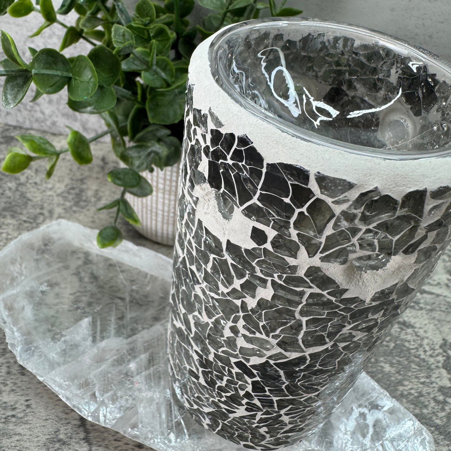 Decorative vase with mosaic pattern on a textured surface with greenery