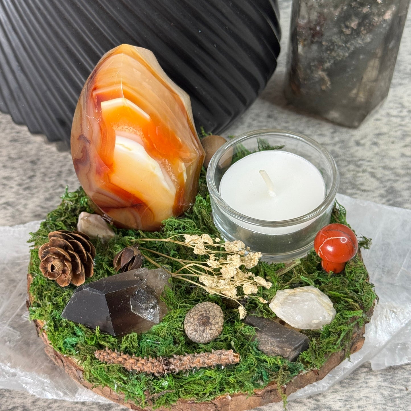 Decorative arrangement with a candle, stones, and natural elements on a textured surface