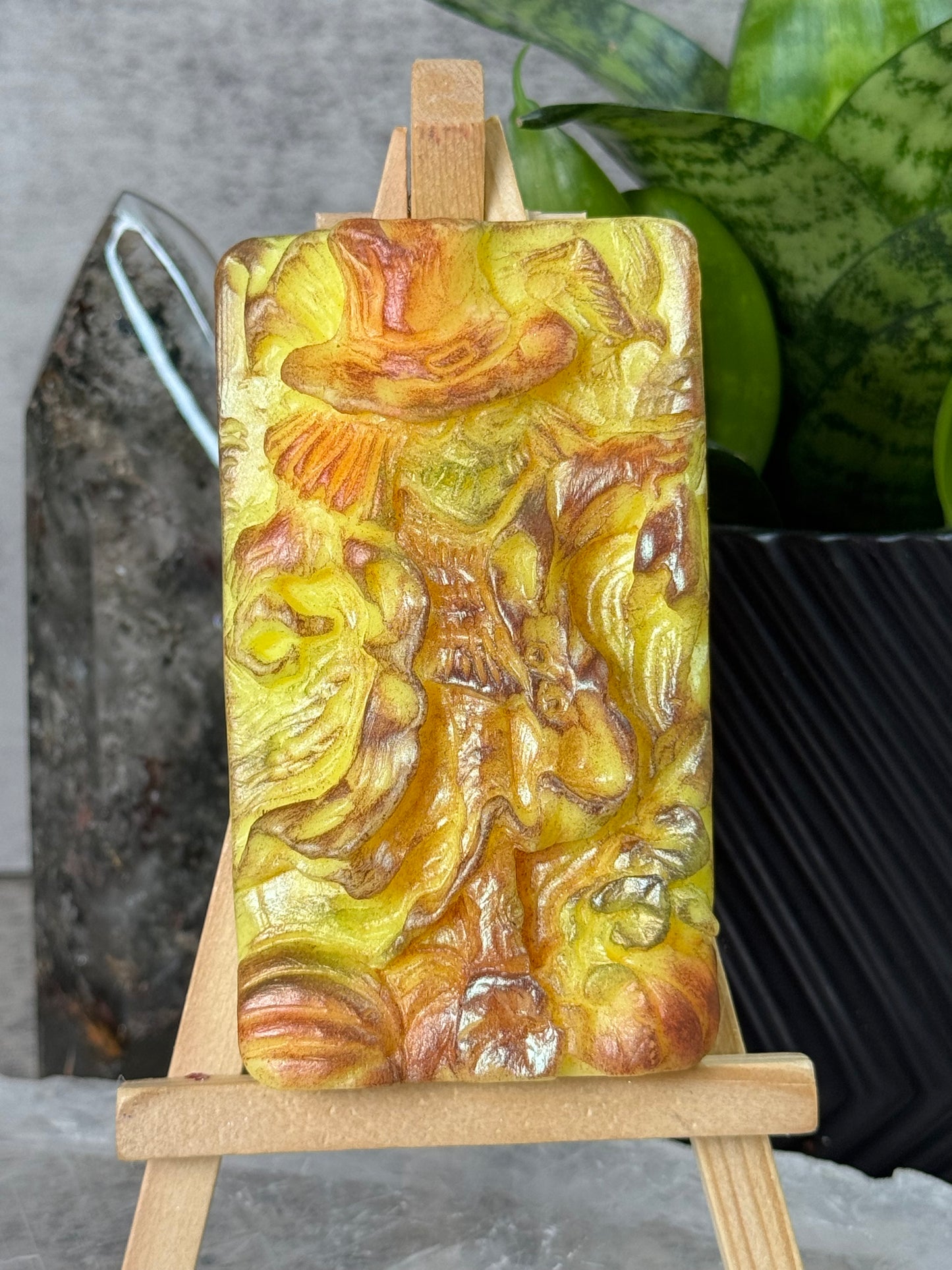 Decorative soap bar with intricate design held by wooden sticks on a gray surface.