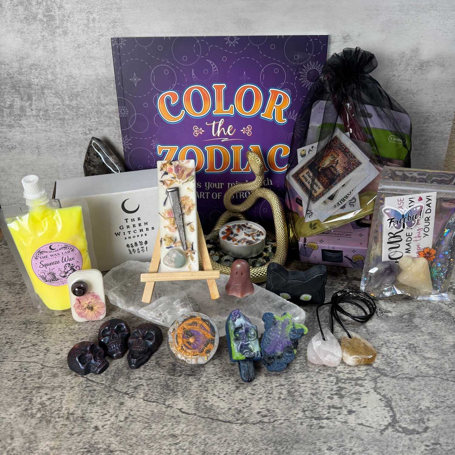Collection of decorative items including a book titled 'Color the Zodiac', crystals, and small sculptures on a textured surface.