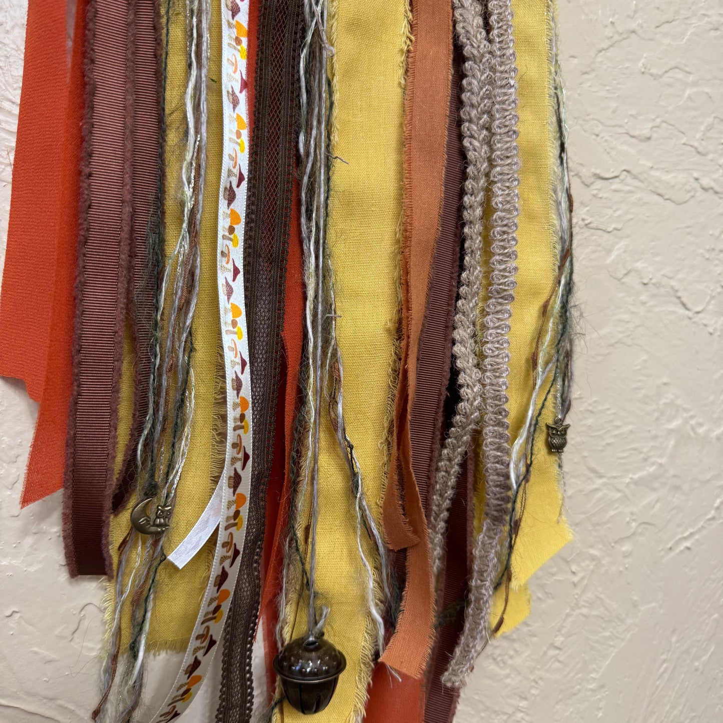 Collection of colorful fabric strips and ribbons on a textured beige wall.
