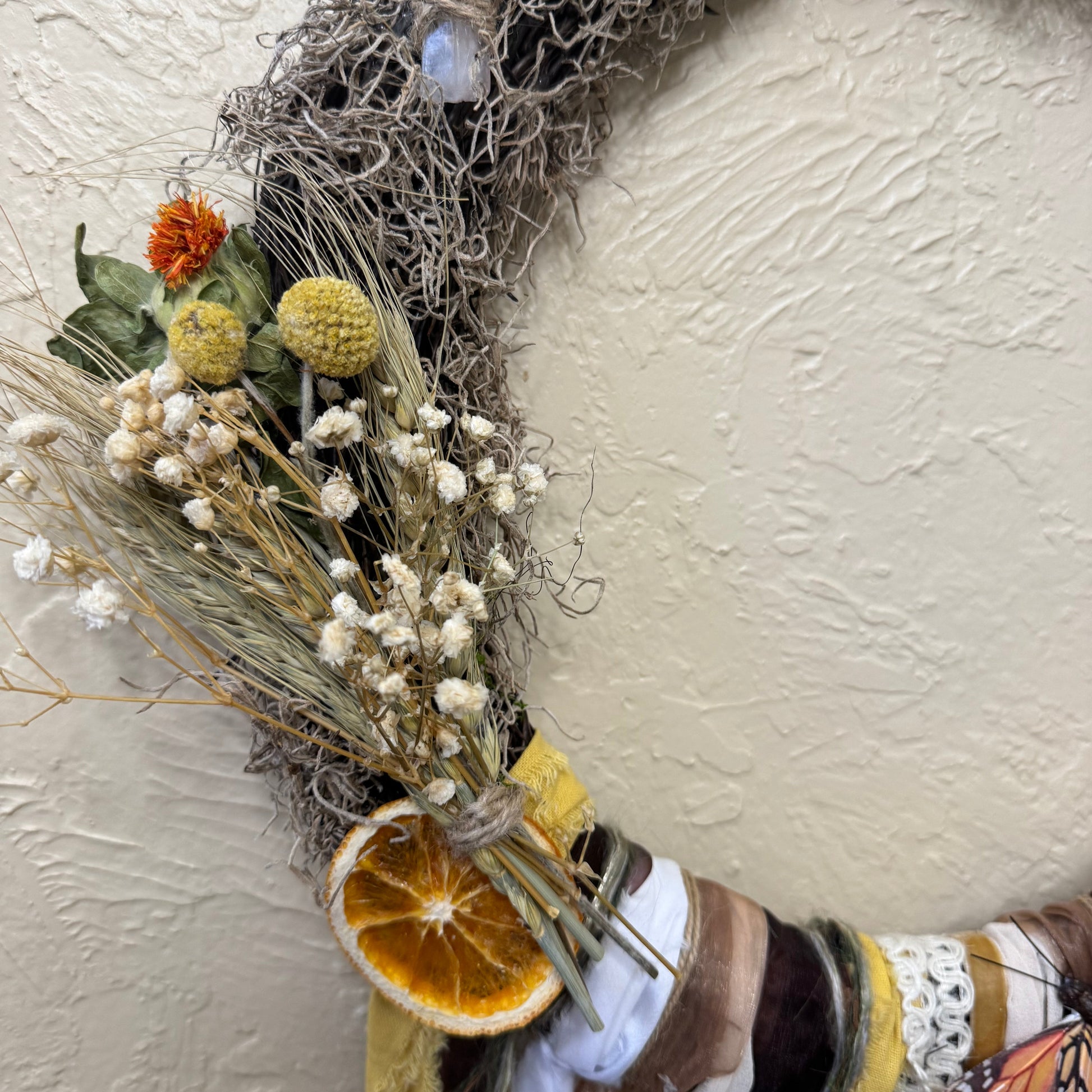 Decorative wreath with dried flowers and an orange slice on a textured white background