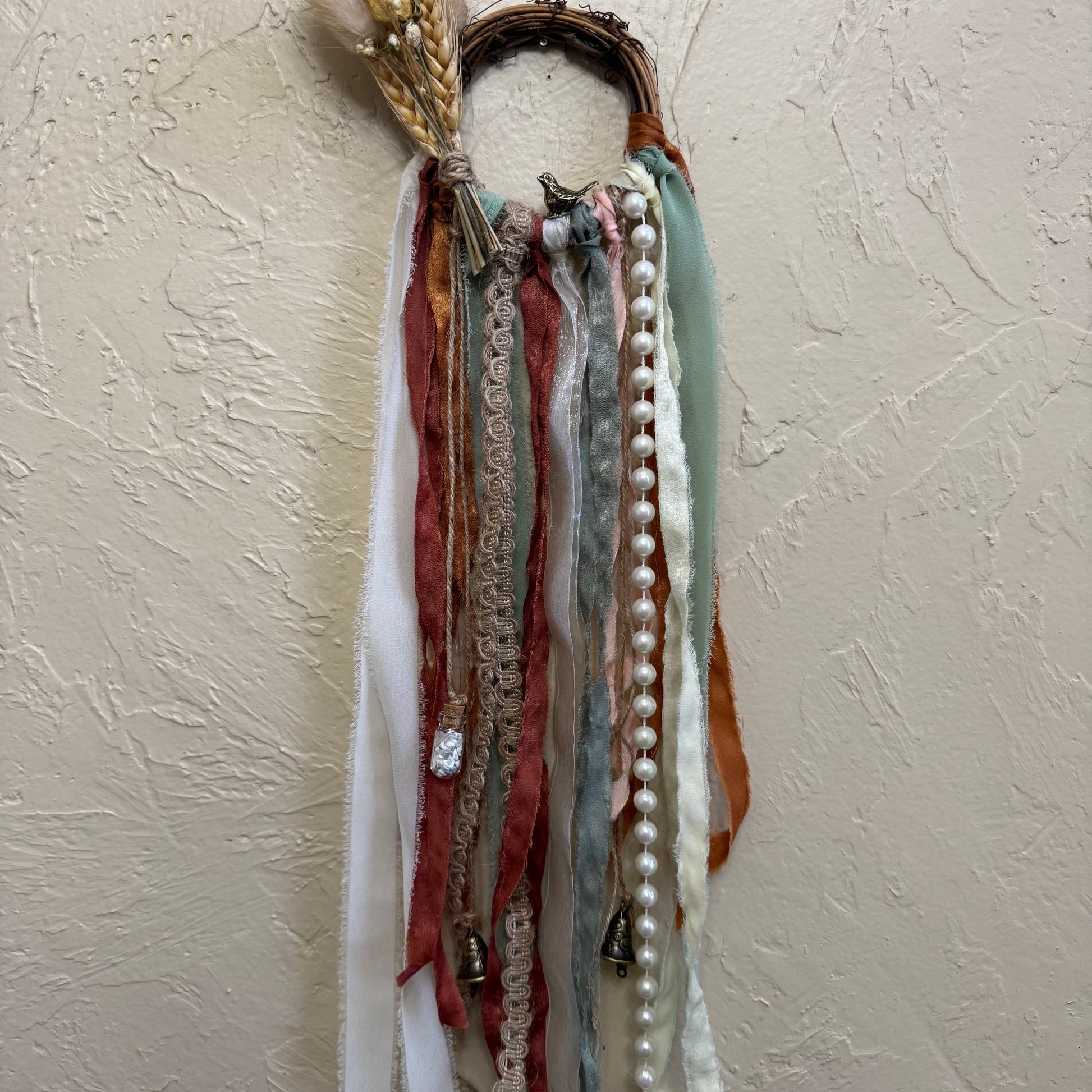 Decorative wall hanging with ribbons and beads on a textured beige wall