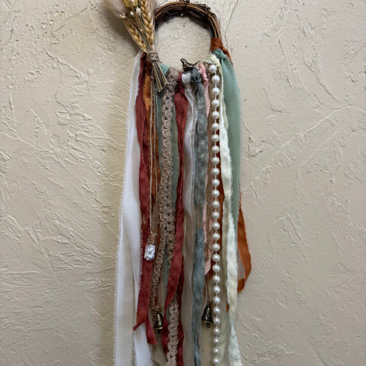 Decorative wall hanging with ribbons and beads on a textured beige wall