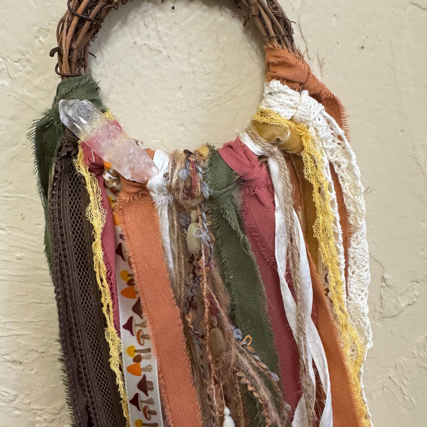 Decorative wreath with fabric strips and a white ball on a textured surface