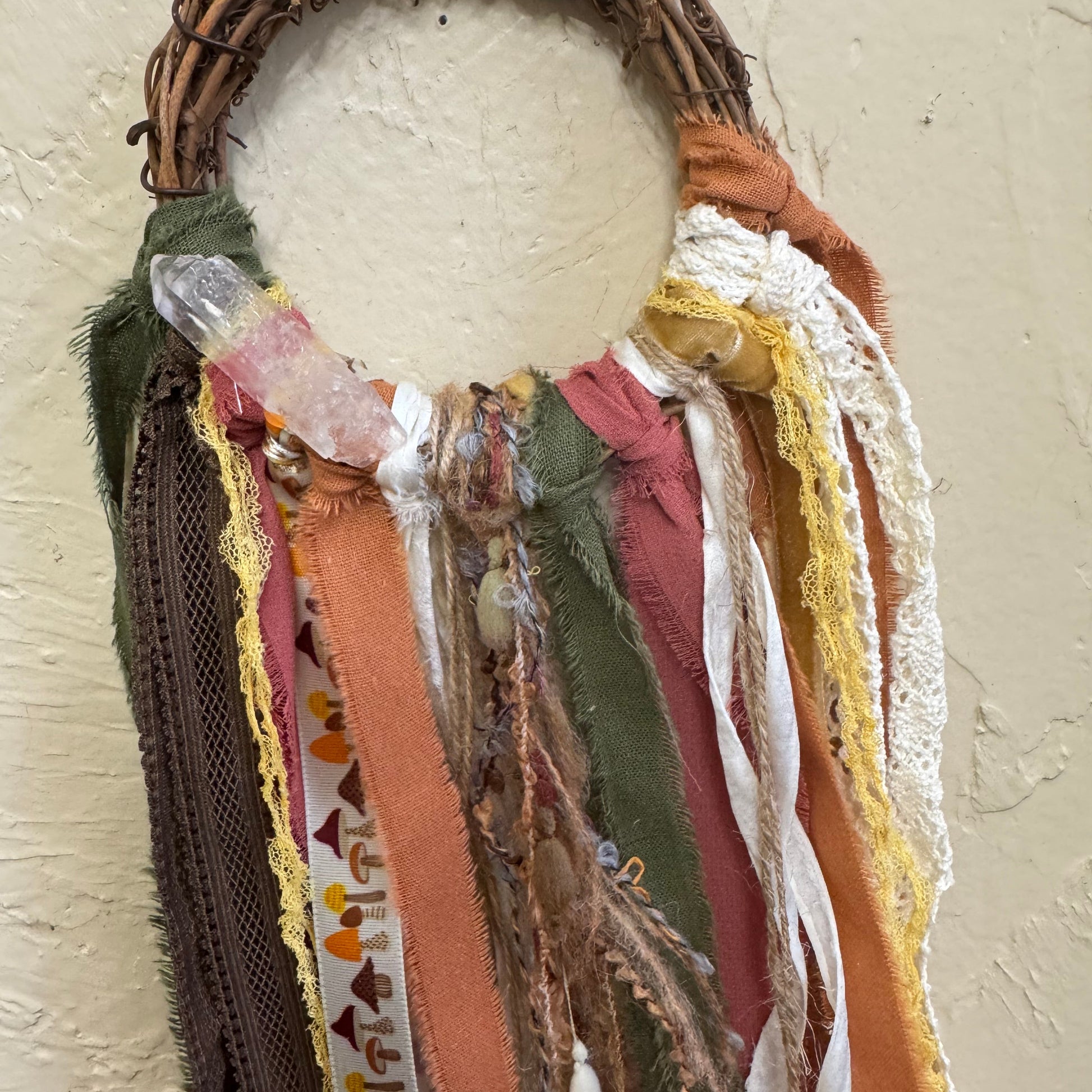 Decorative wreath with fabric strips and a white ball on a textured surface