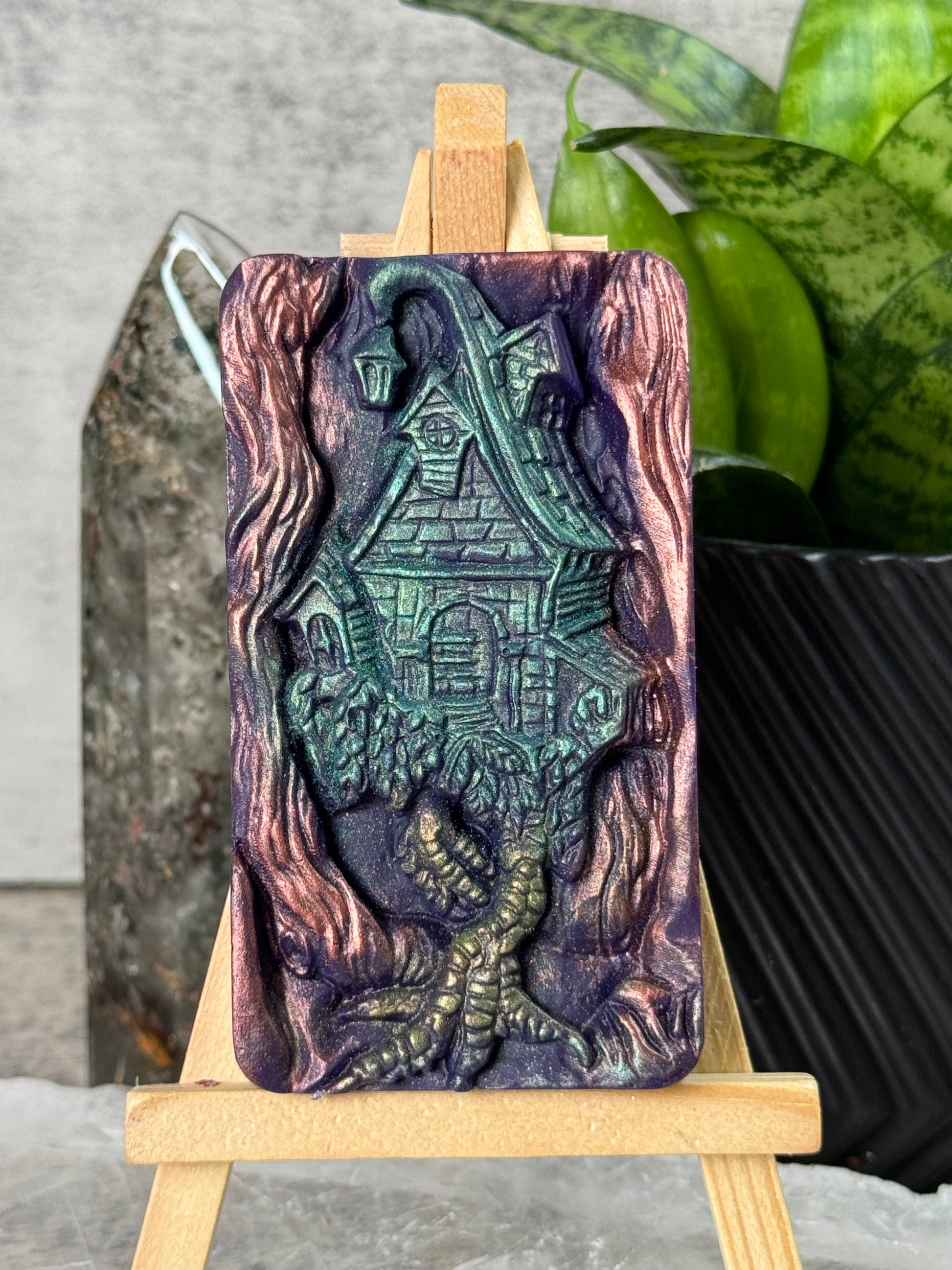 Decorative soap bar with intricate design on a wooden stand, plant and black bag in the background.