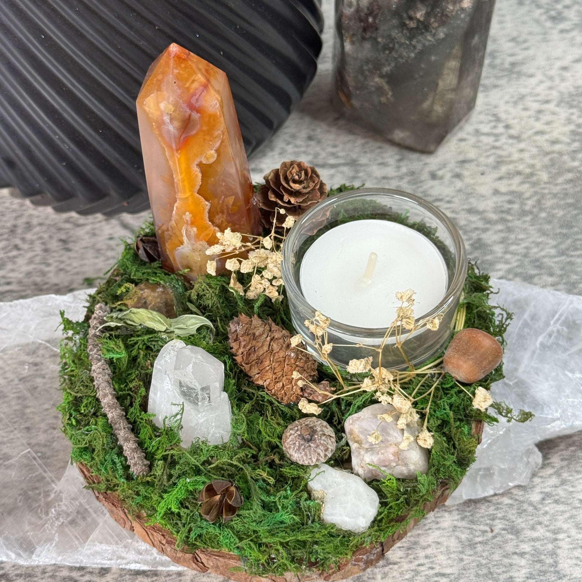 Decorative arrangement with a candle, crystals, and moss on a stone surface