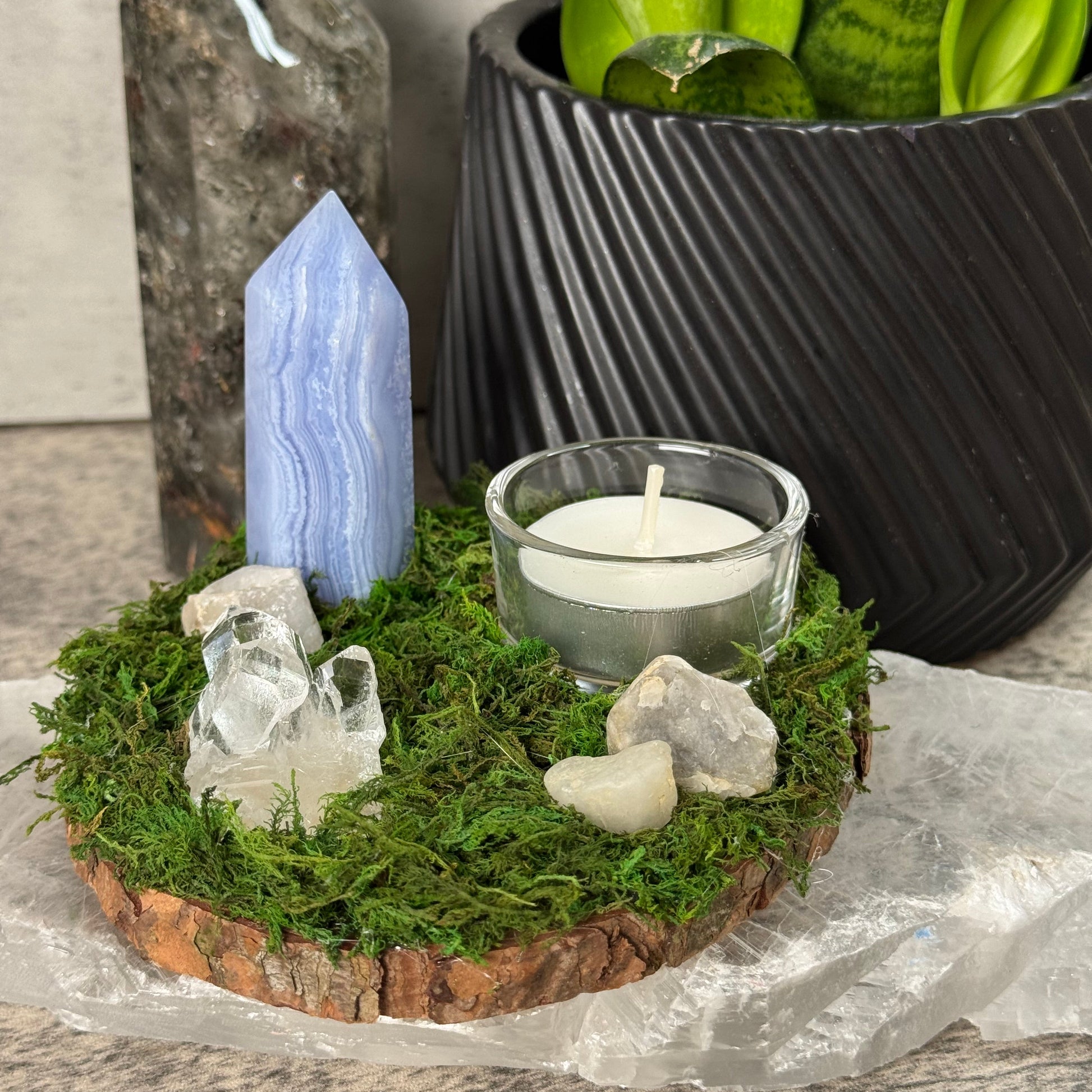 Decorative setting with a candle, crystals, and greenery on a stone surface