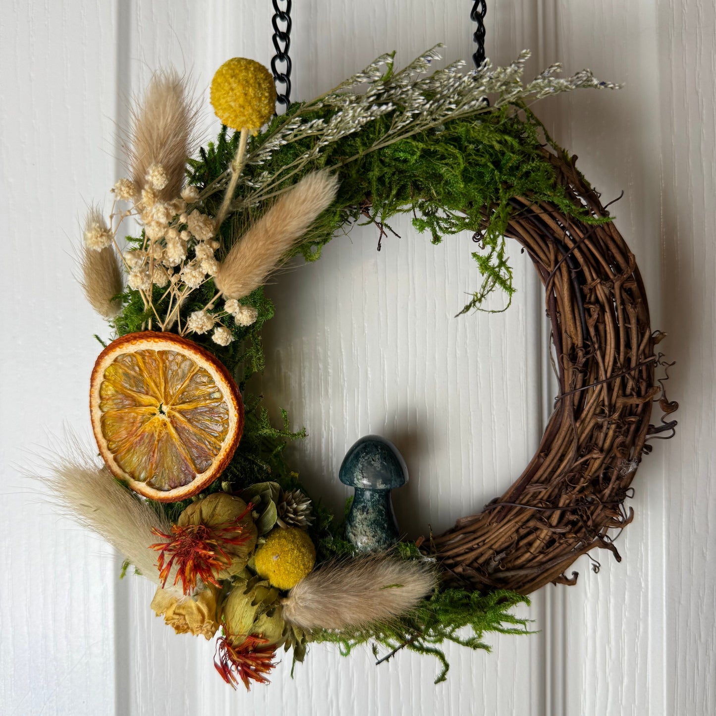 Decorative wreath with dried flowers, a mushroom, and an orange slice on a white wooden door.