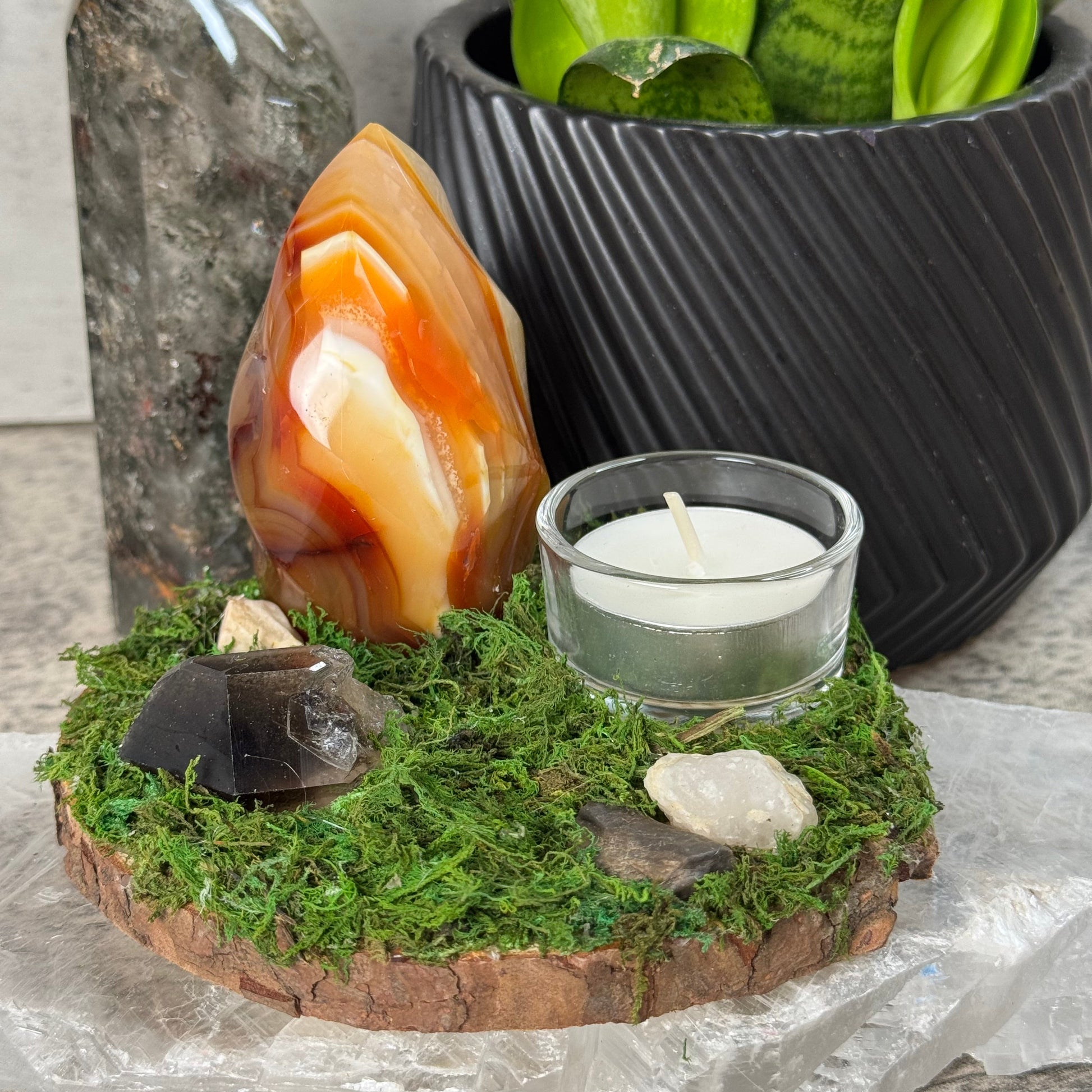 Decorative setting with a candle, agate stone, and moss on a stone surface.