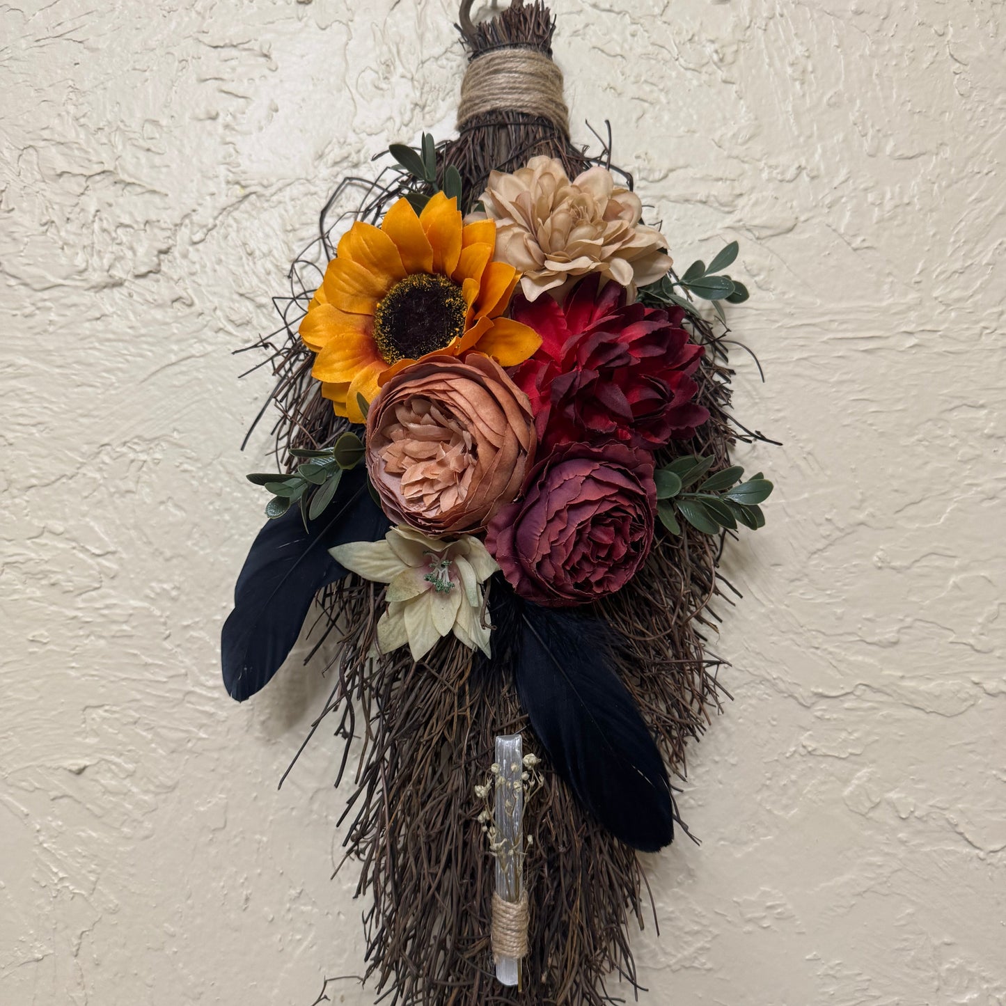 Decorative broom with autumnal flowers against a textured white wall
