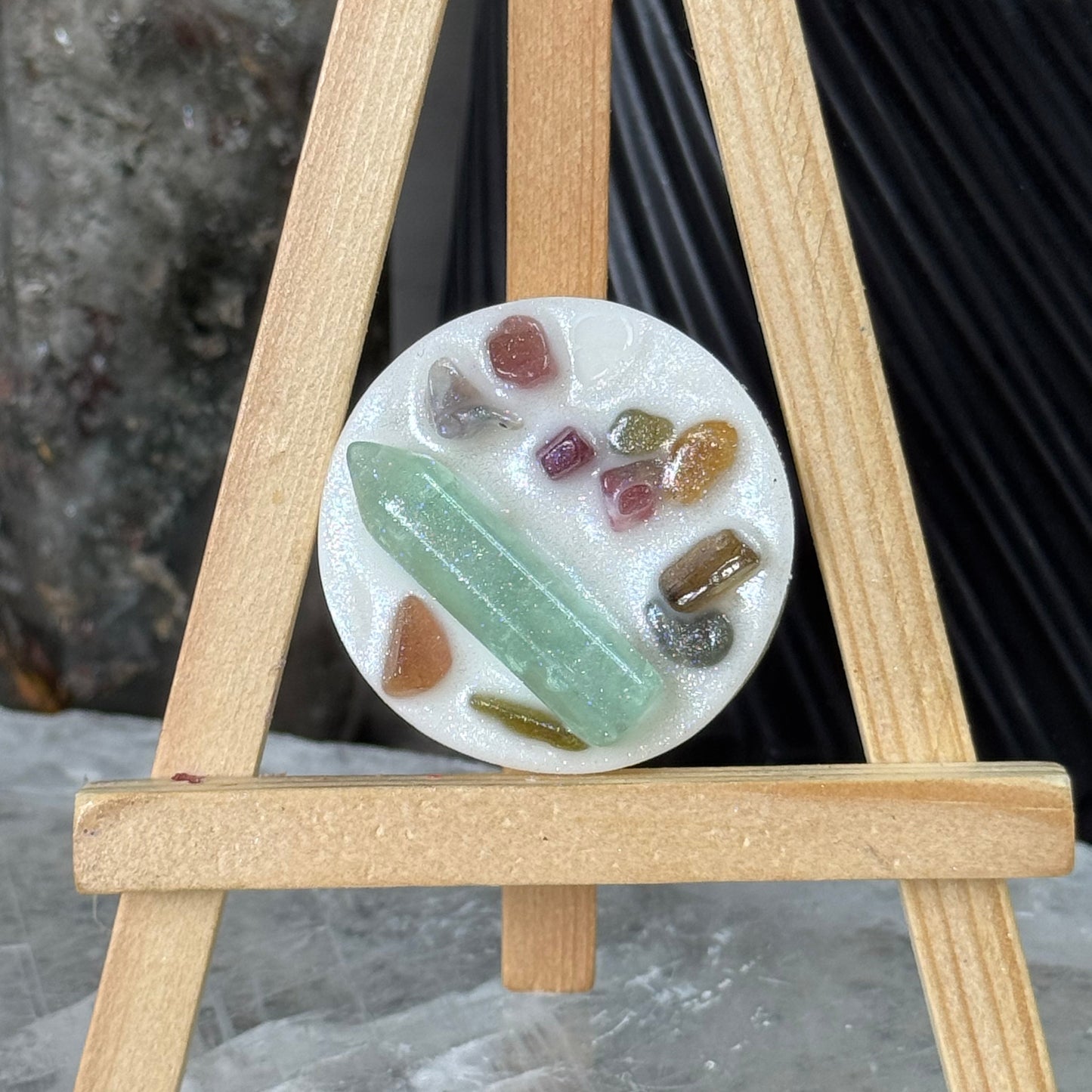 Round stone sample with various colors on a white background, held by wooden sticks.