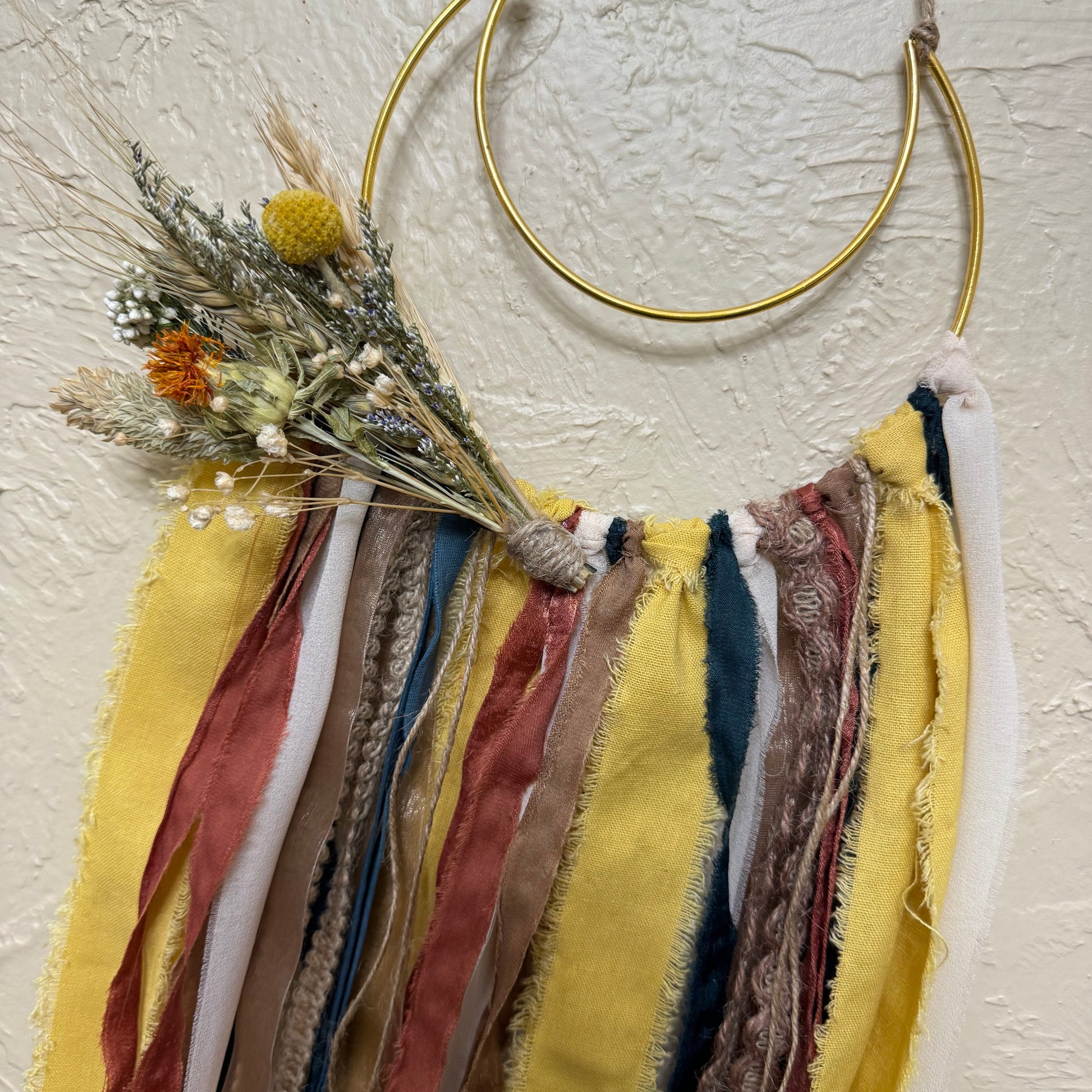 Decorative wall hanging with ribbons and dried flowers on a textured wall.