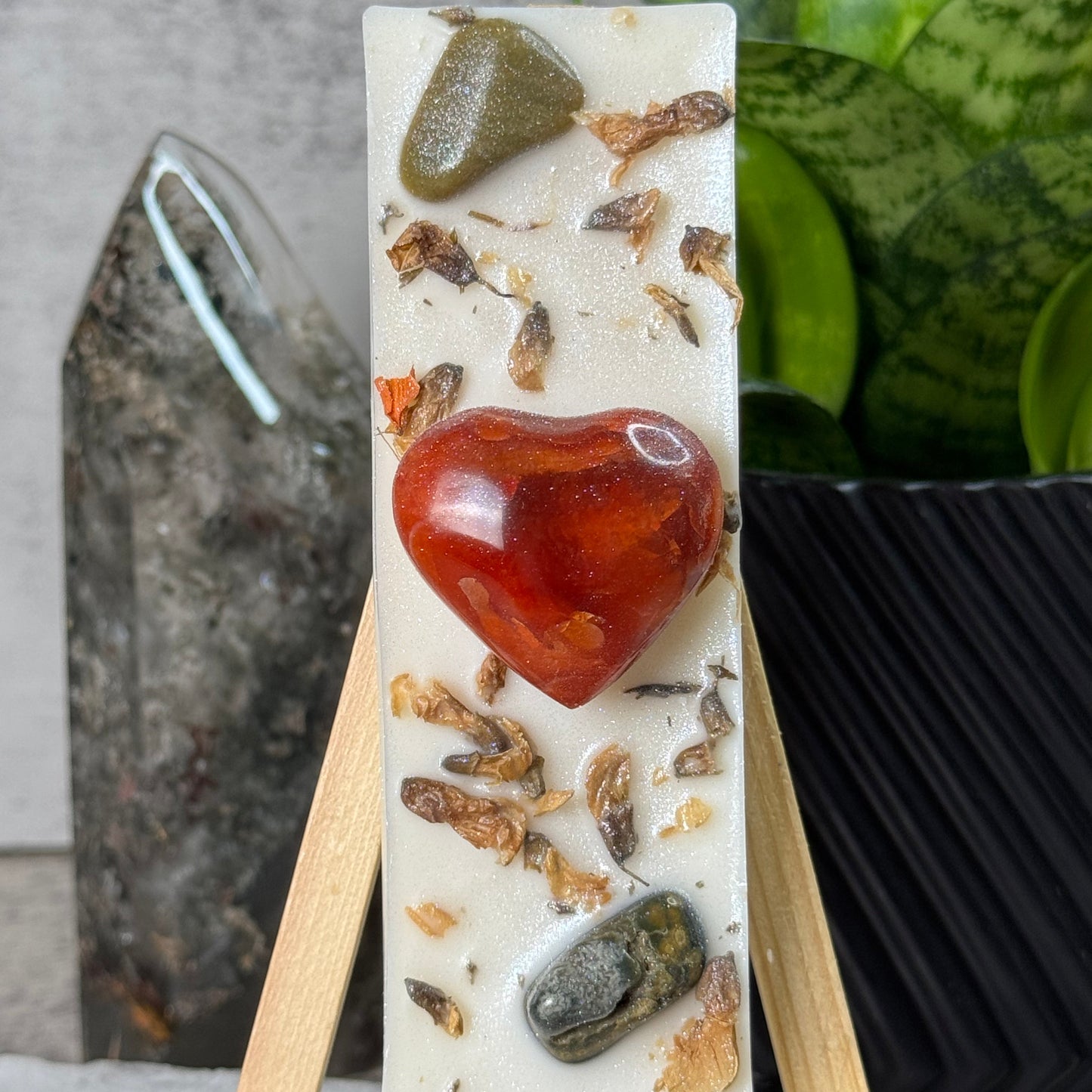 Decorative soap bar with natural elements on a stand, plant and marble surface in the background