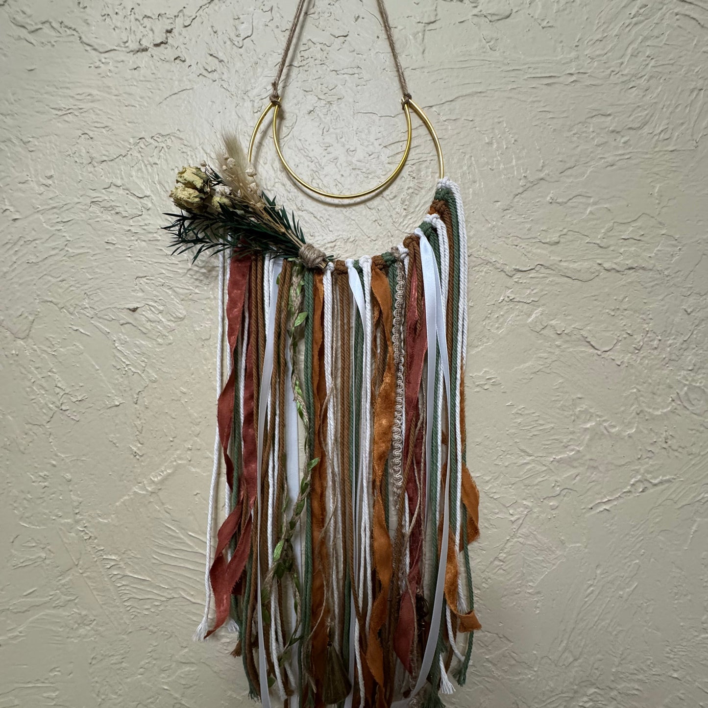 Decorative wall hanging with feathers and ribbons on a textured white wall
