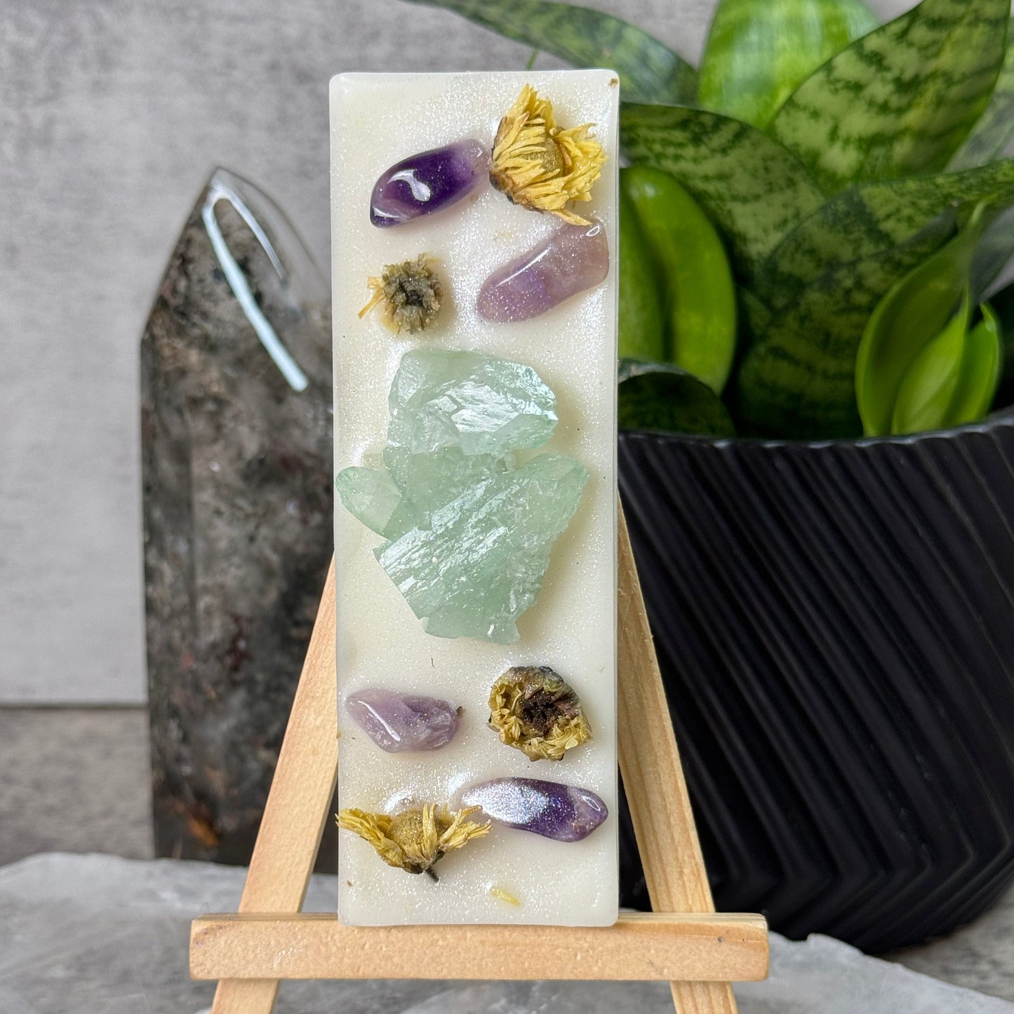 Decorative soap with embedded crystals and flowers on a stand, against a neutral background.