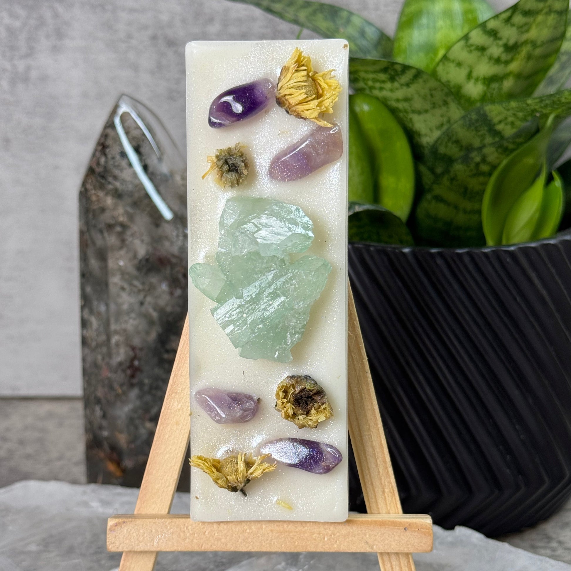 Decorative soap with embedded crystals and flowers on a stand, against a neutral background.