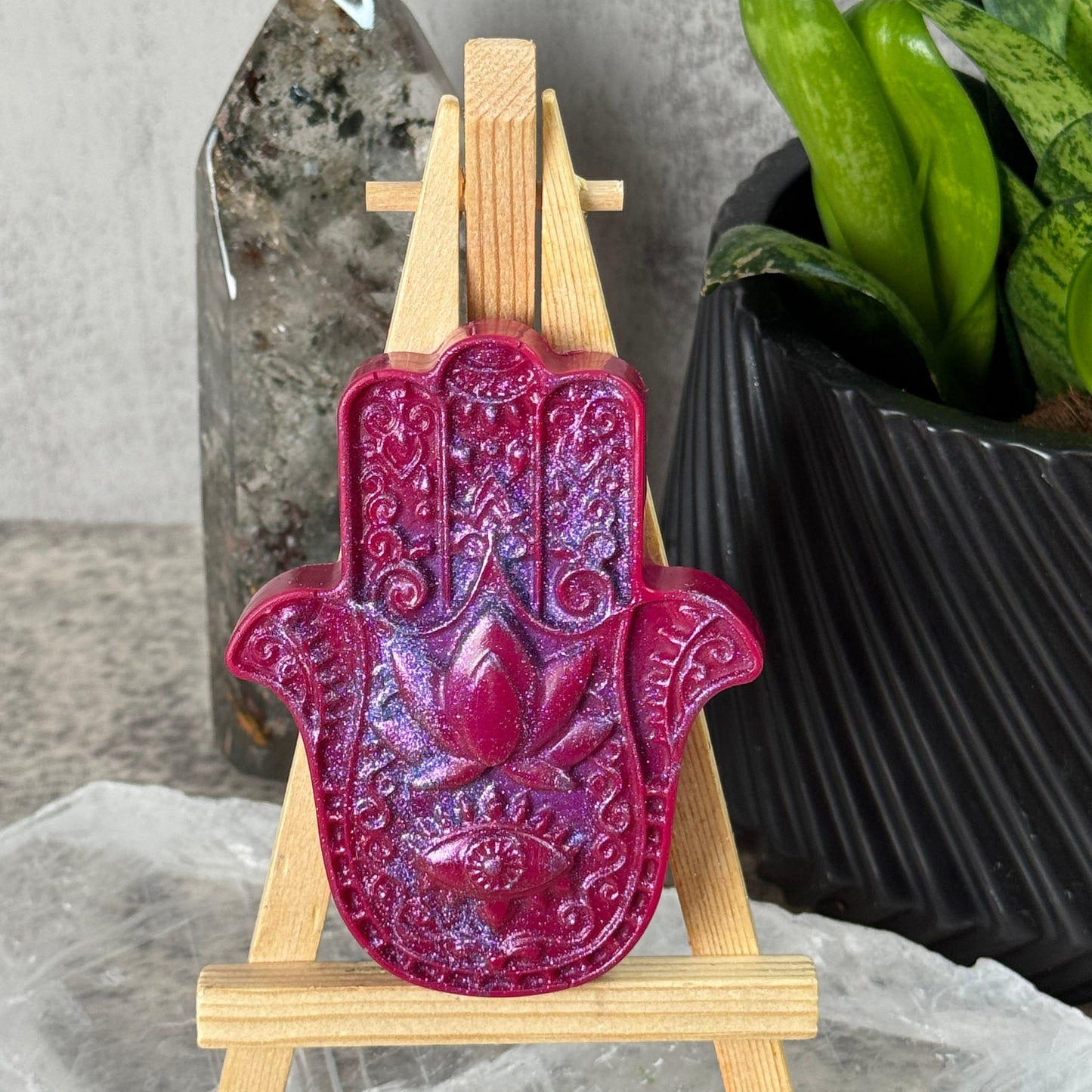 Pink Hamsa hand on a wooden stand with green leaves and a stone background