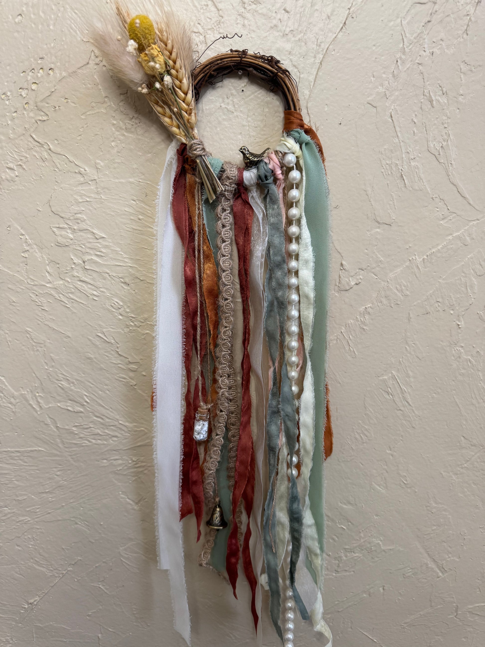 Decorative wall hanging with ribbons and beads on a textured beige wall