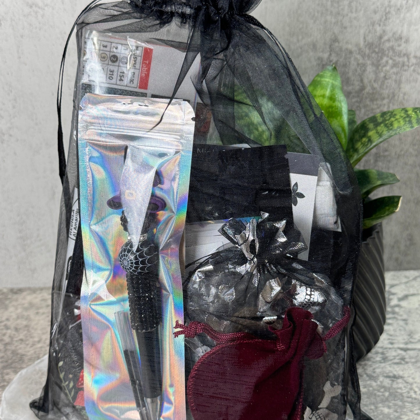 Black gift bag with decorative items including a metallic pen and black card on a neutral background.