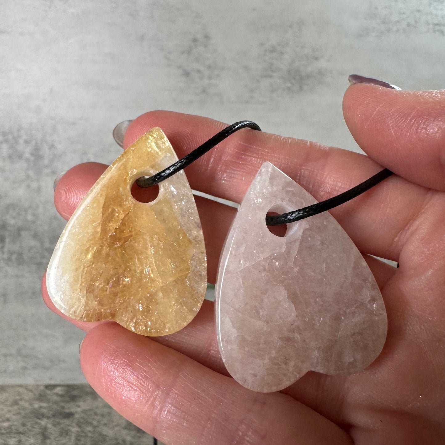 Heart-shaped stone pendants held in a hand against a neutral background