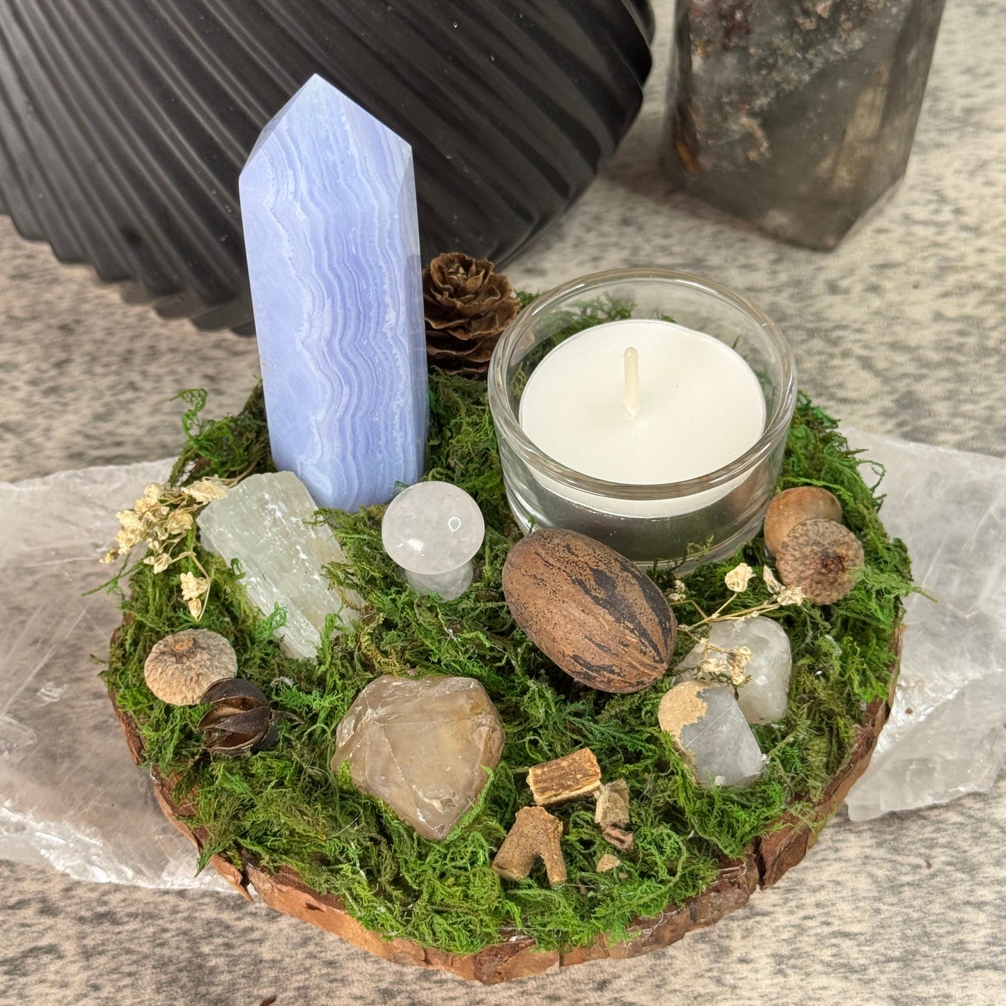 Mossy stone bowl with a candle, crystals, and a crystal point on a textured surface.