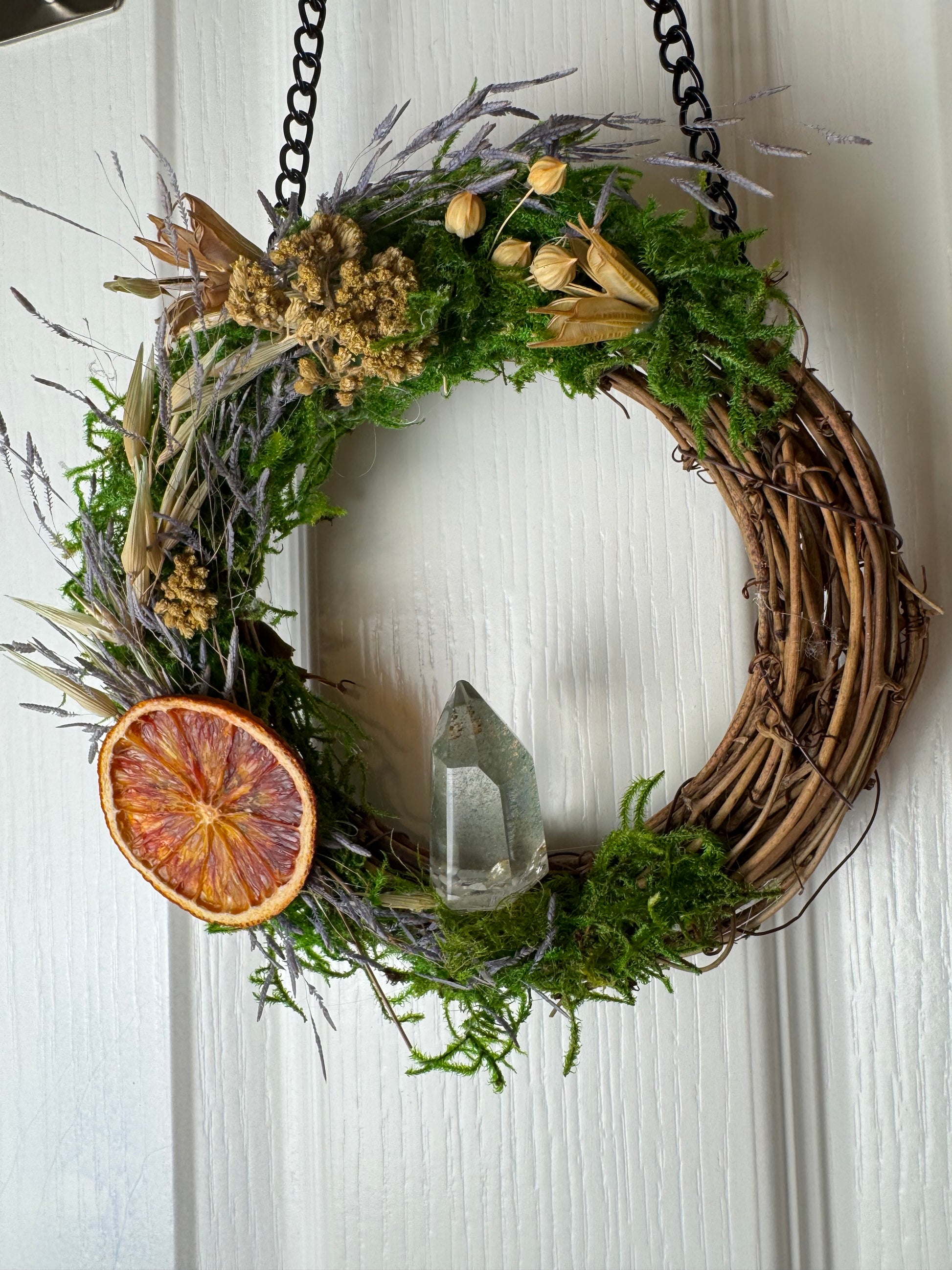 Decorative wreath with greenery, dried oranges, and a crystal on a white background