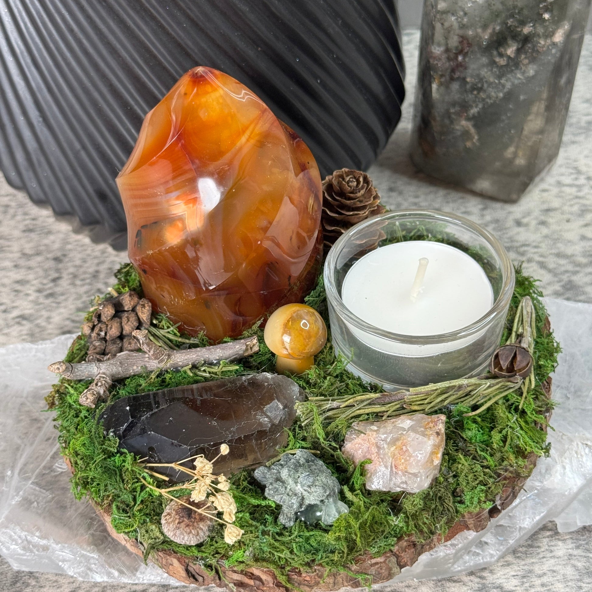 Decorative arrangement with a candle, stones, and plants on a stone surface