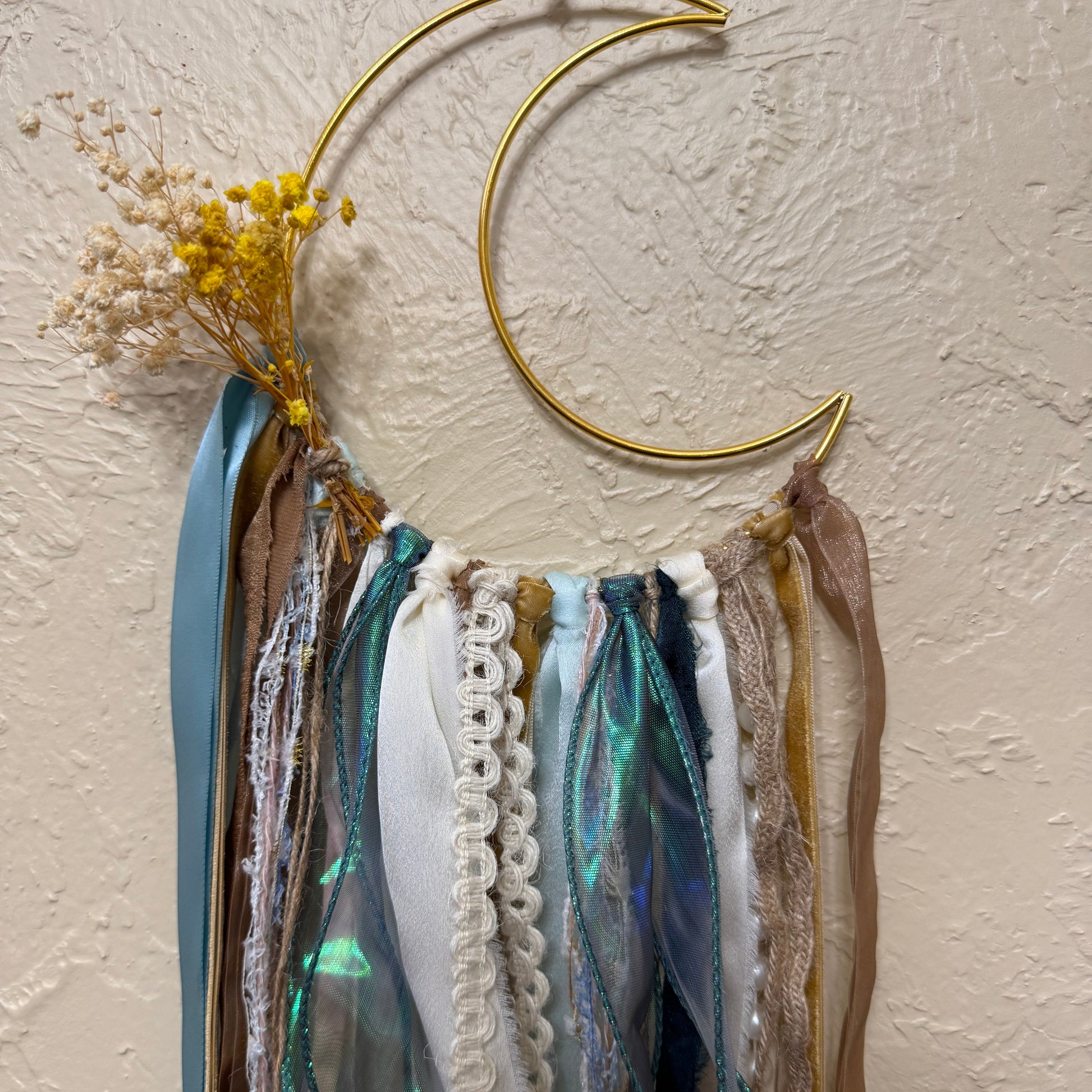Gold crescent moon necklace displayed on a textured surface with a mirror and feathers.