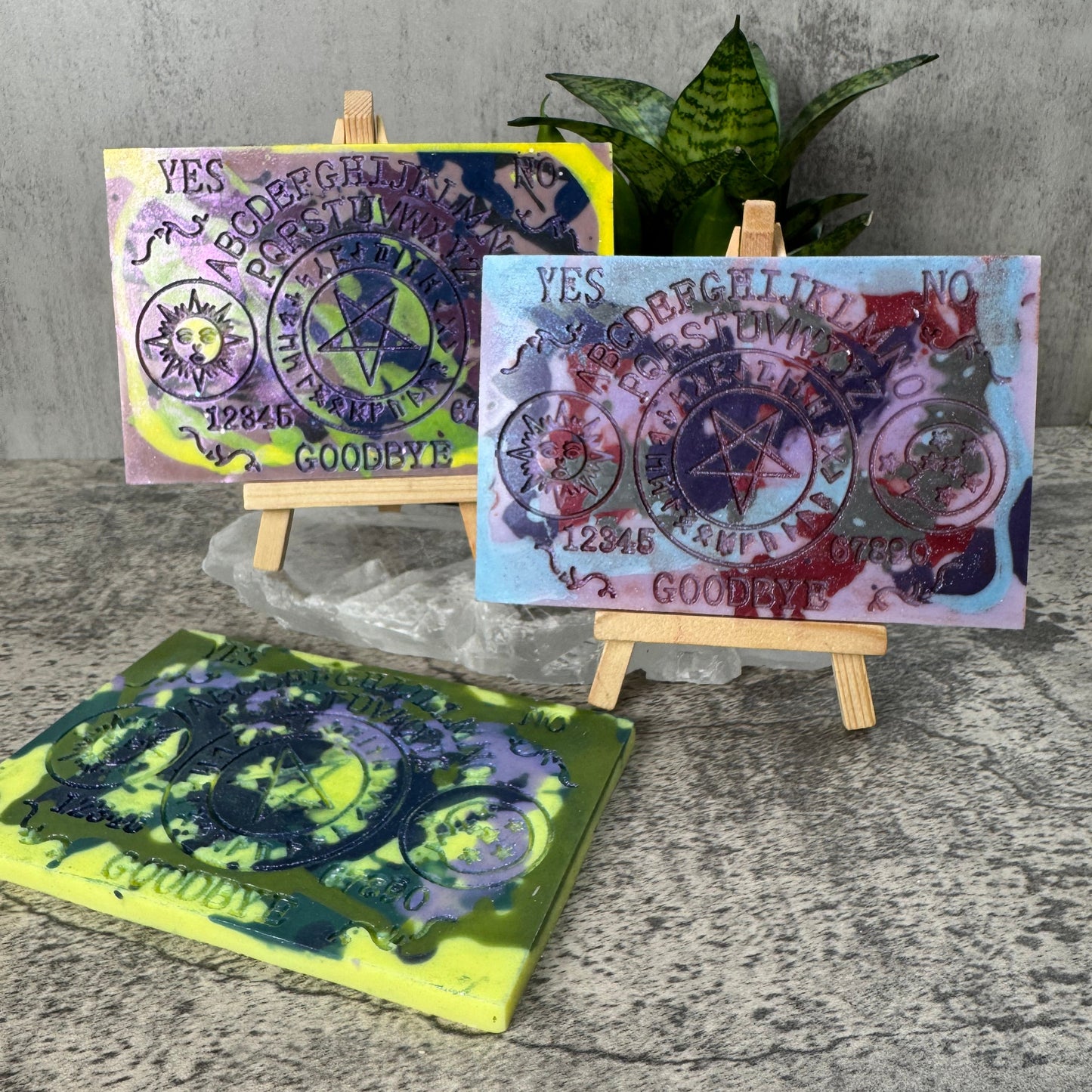 Three colorful tarot cards on a stand with a plant and textured surface in the background