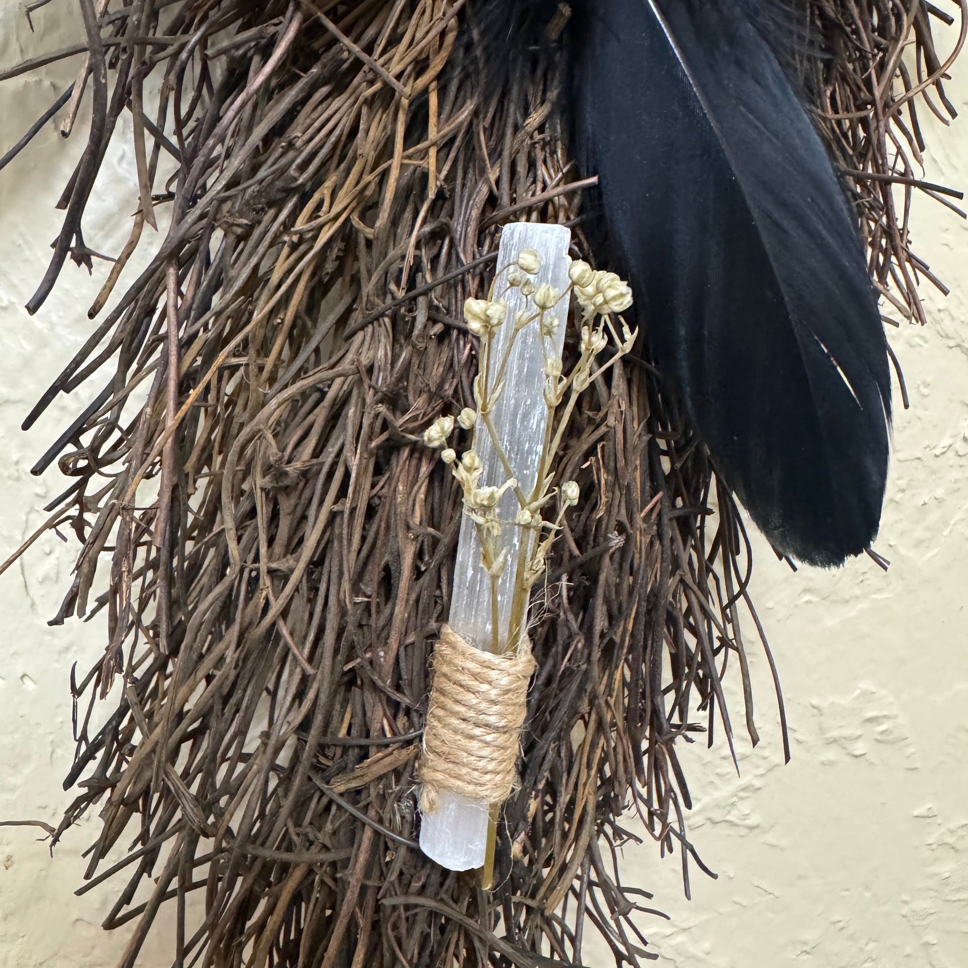 Decorative arrangement with black feather, dried flowers, and twigs on a textured surface