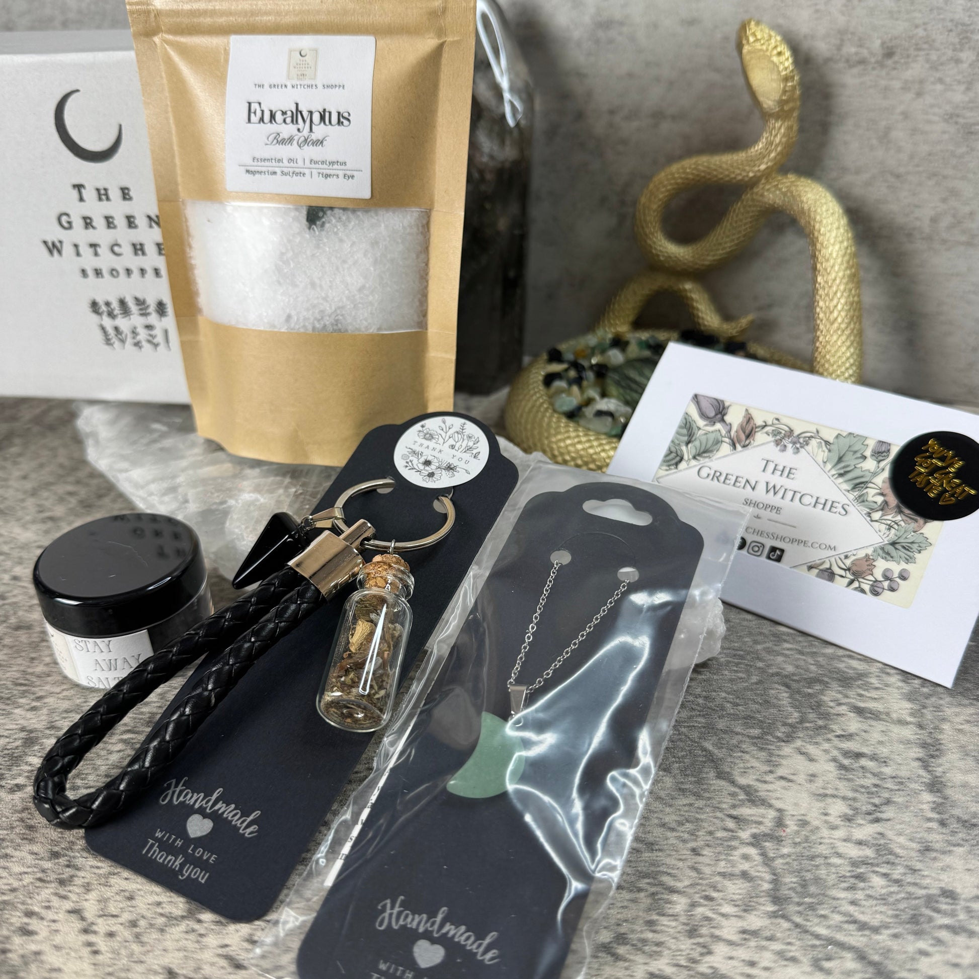 Collection of wiccan or pagan products including a bag of Epsom salts, a jar, a keychain, and a hairbrush on a textured surface.