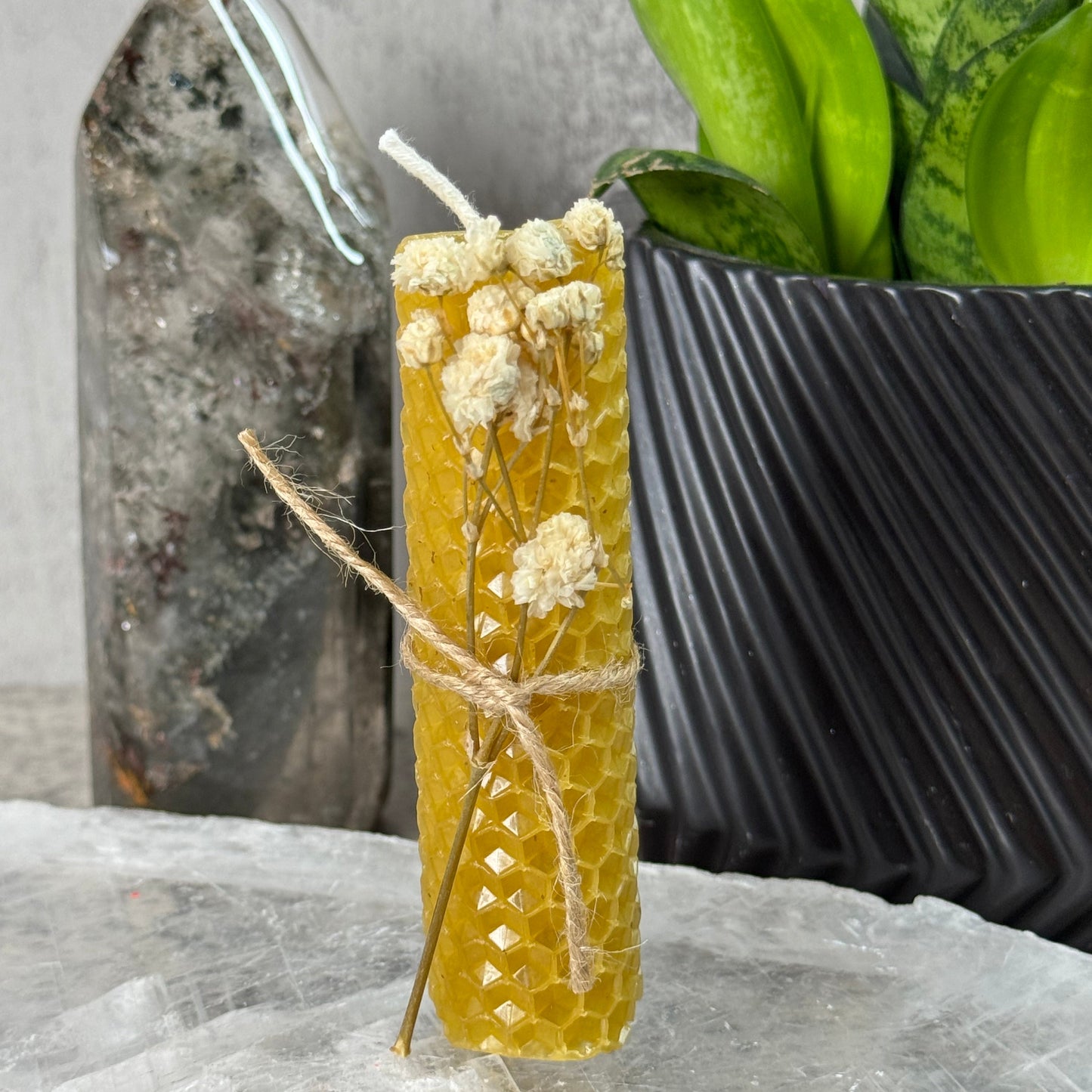 Yellow candle with floral design tied with twine on a stone surface with a plant in the background