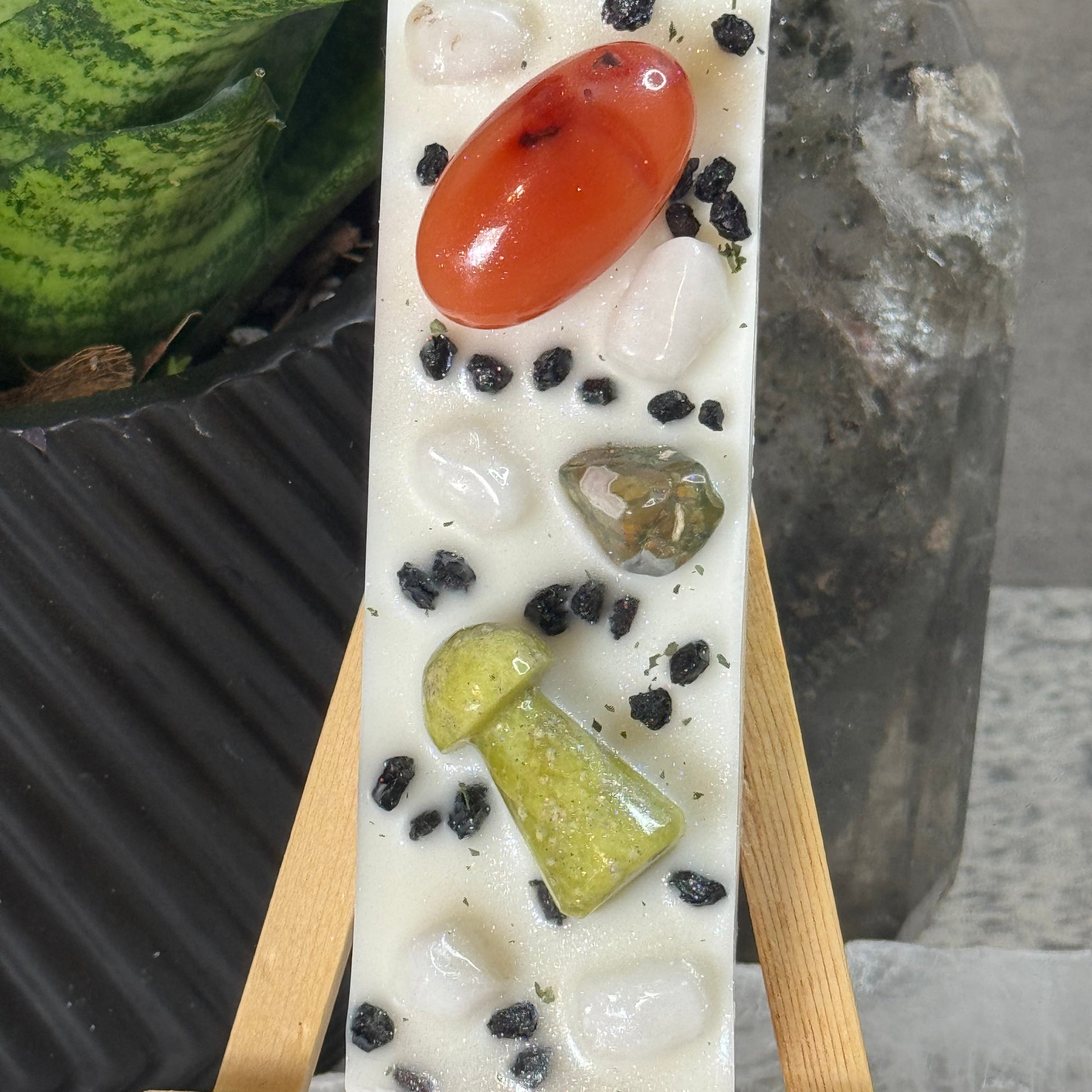 Rectangular soap with embedded stones and a red stone on a wooden stand against a neutral background