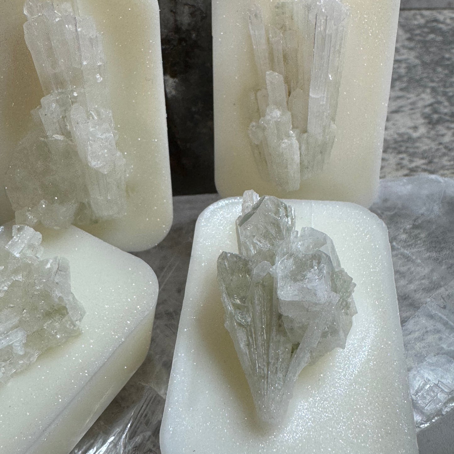 Three rectangular white foam blocks, each with a clear crystal cluster embedded or placed on top, arranged on a crinkled clear plastic sheet. The crystals are translucent and natural-looking.