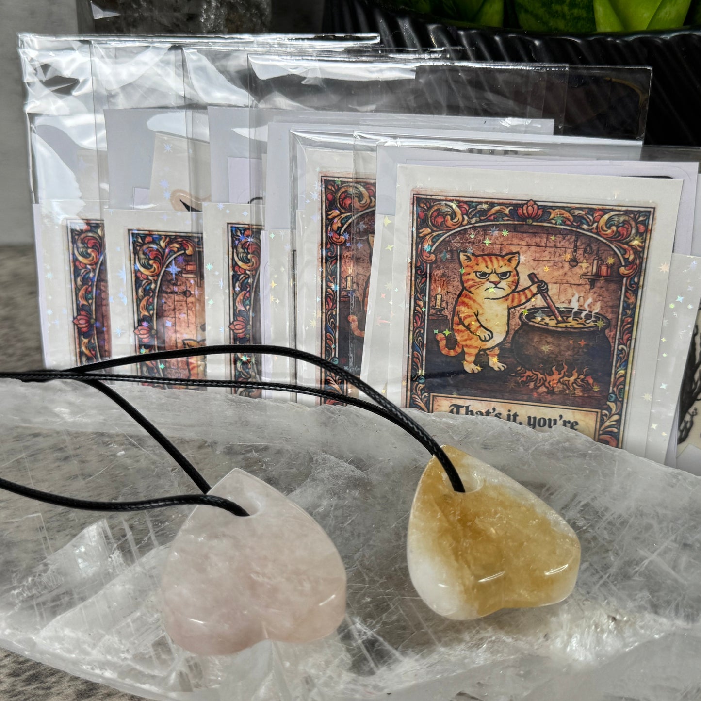Two stone pendants on a black cord with cards featuring cat illustrations in the background.