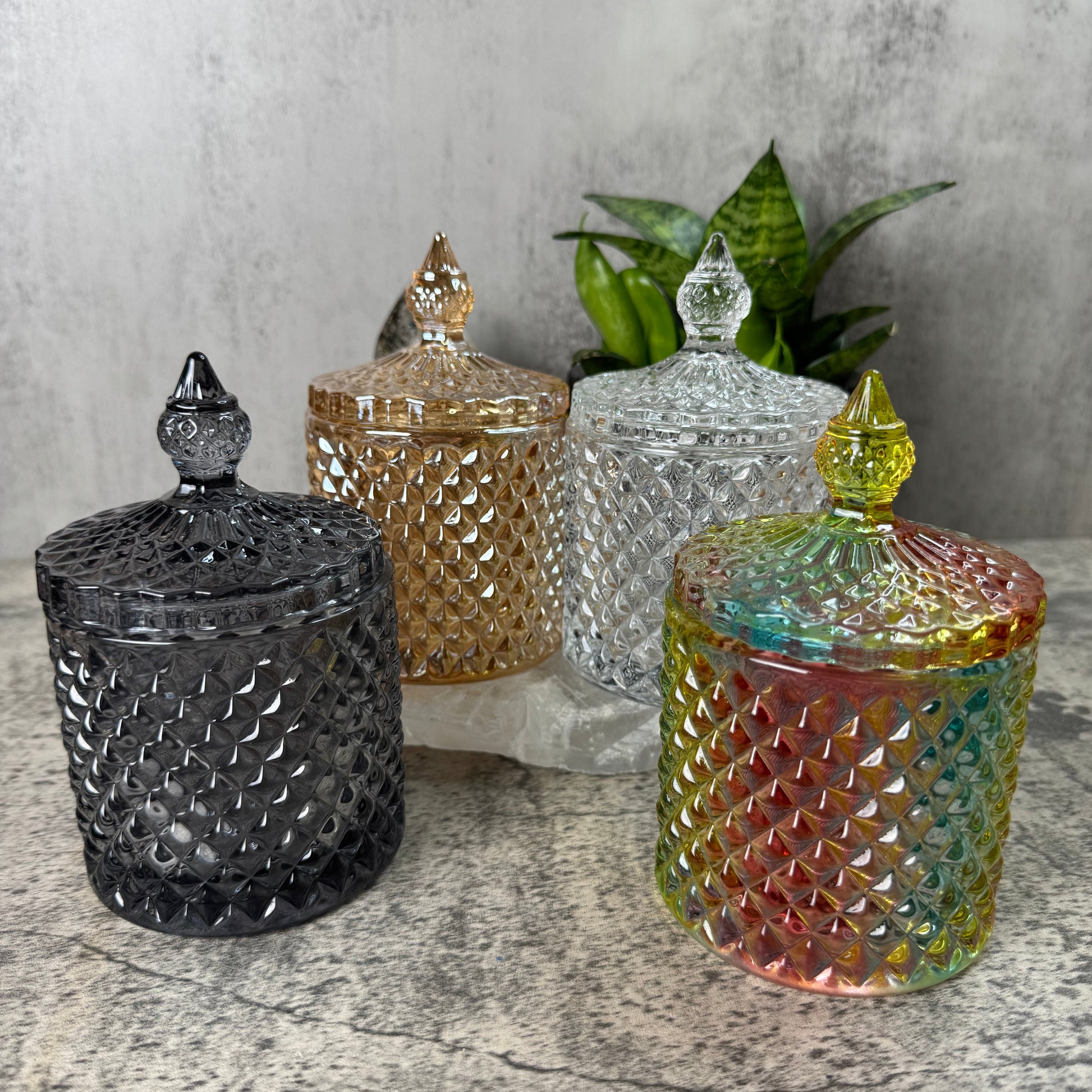Four colorful glass jars with textured lids on a stone surface with a gray concrete wall background.