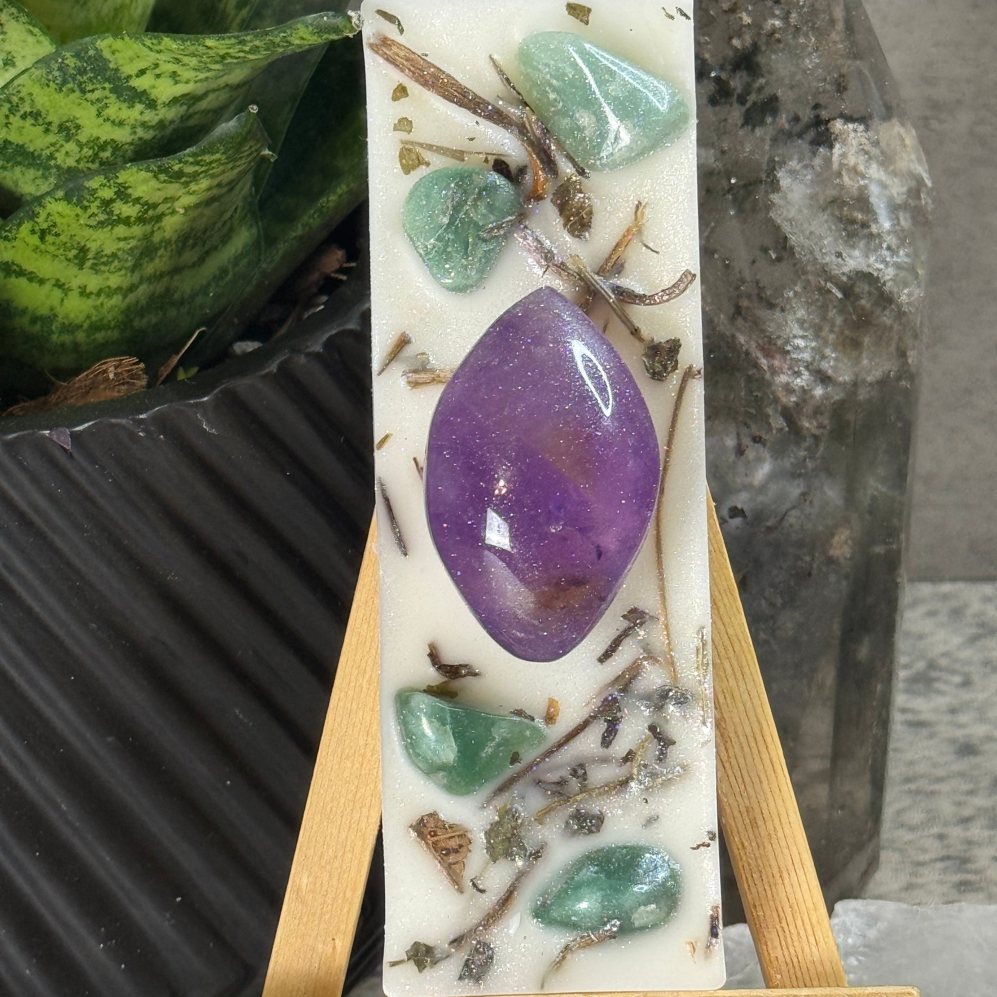 Soap bar with natural elements and a purple stone on a wooden stand, with a neutral background.
