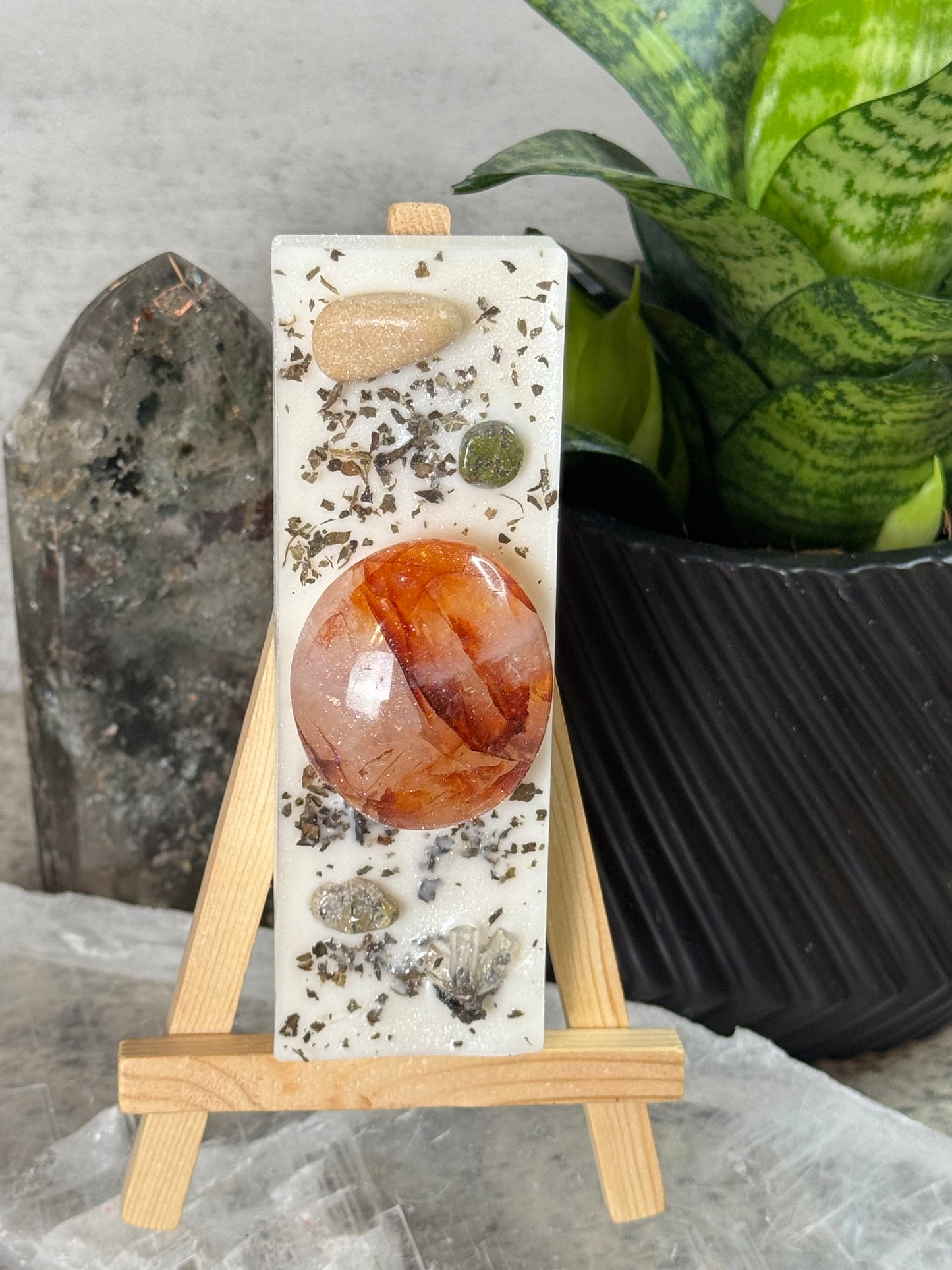 Decorative stone with a large red stone on a wooden stand, surrounded by plants and stones.