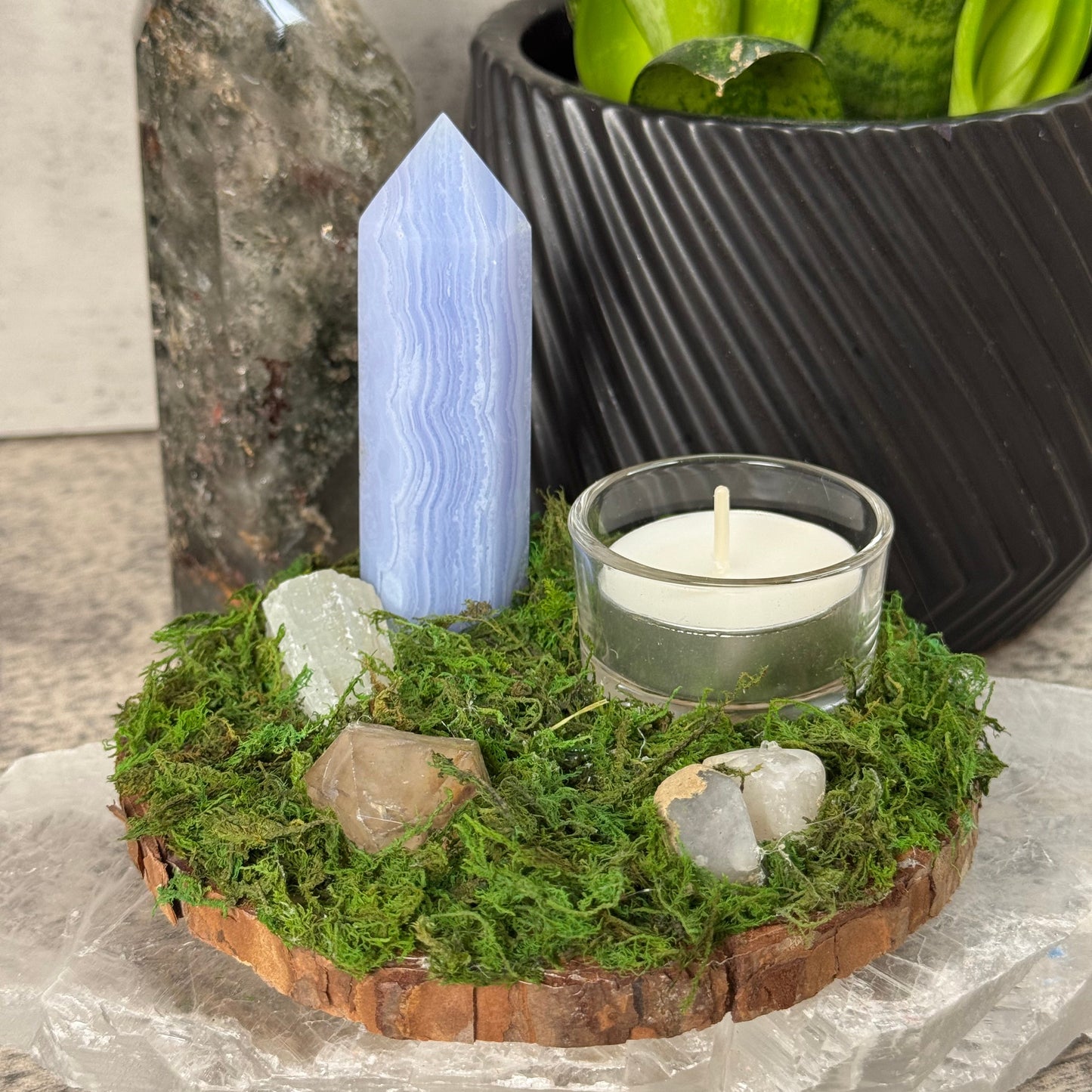 Moss-covered stone with a candle and crystals on a gray surface