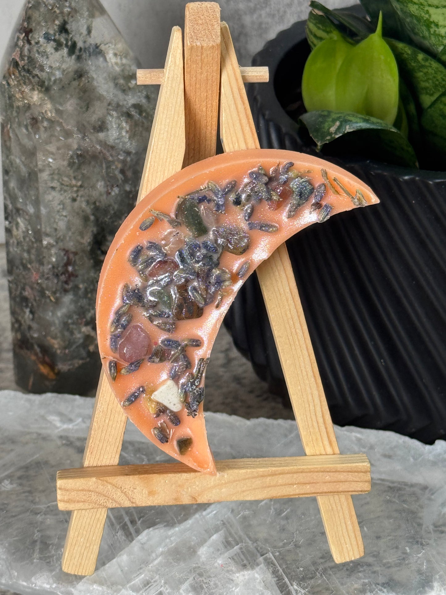 Decorative moon-shaped piece with embedded stones on a wooden stand against a gray stone background.