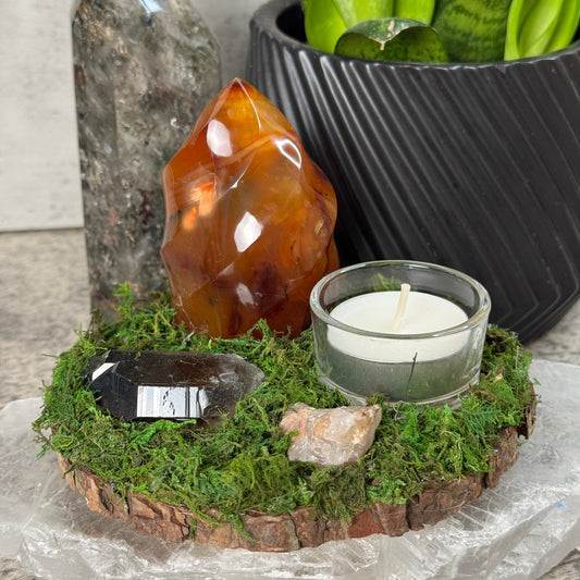 Decorative arrangement with crystals, a candle, and plants on a textured surface.