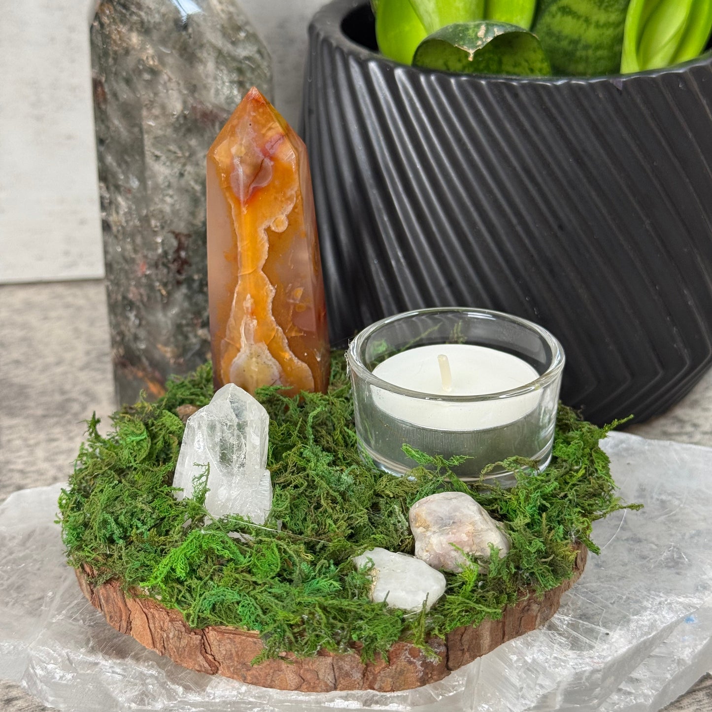 Decorative arrangement with crystals, candle, and plants on a stone surface
