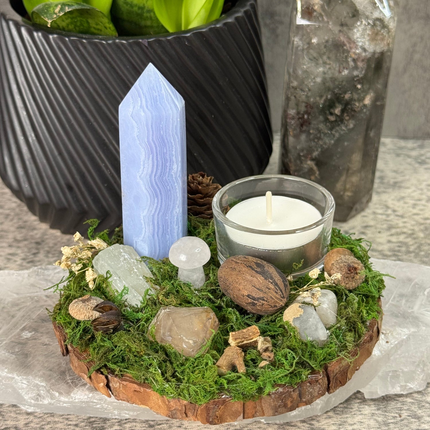 Mossy wreath with a candle, crystals, and stones on a stone surface.